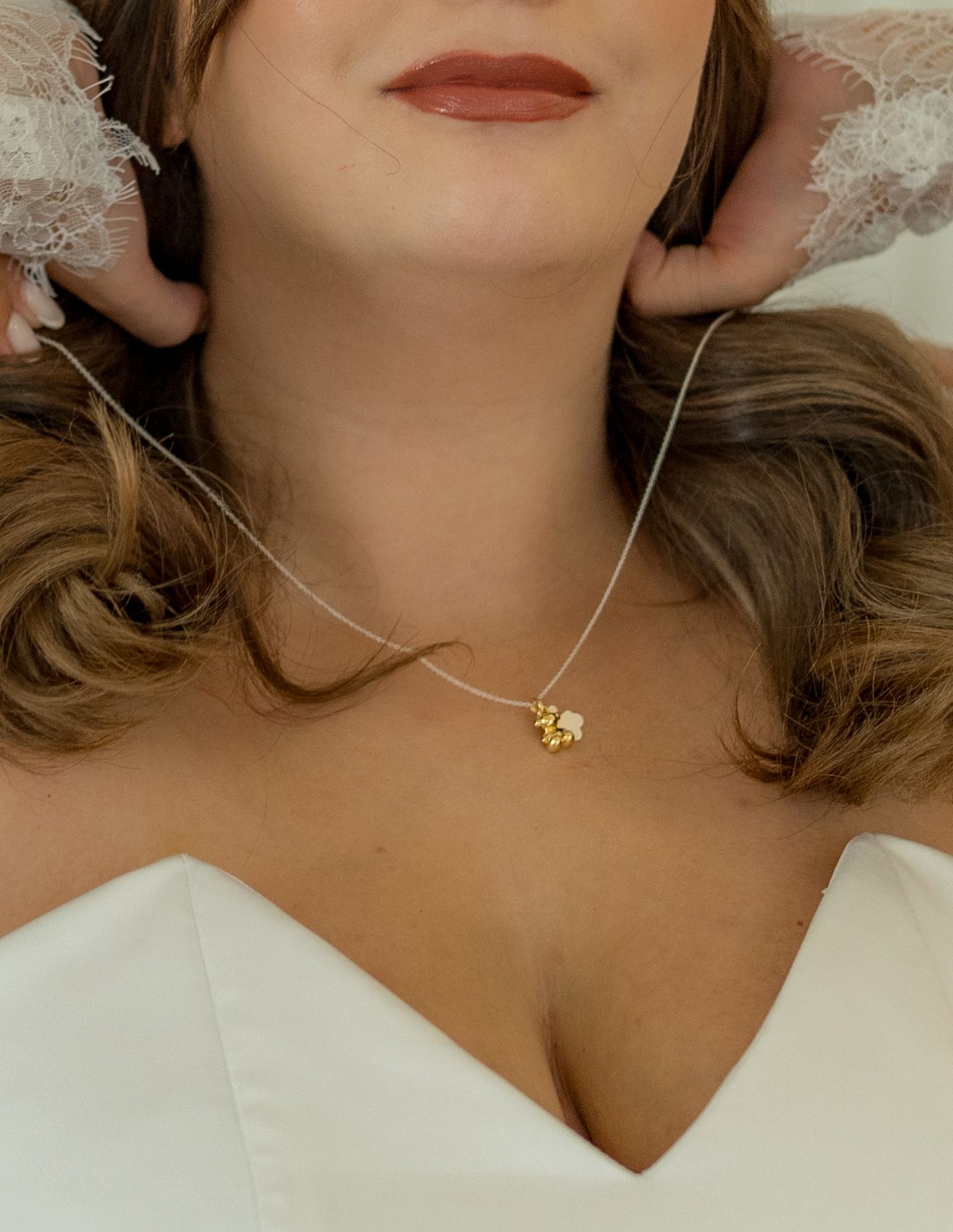 Bride wearing a delicate gold flower pendant necklace on a thin chain with a white wedding dress.