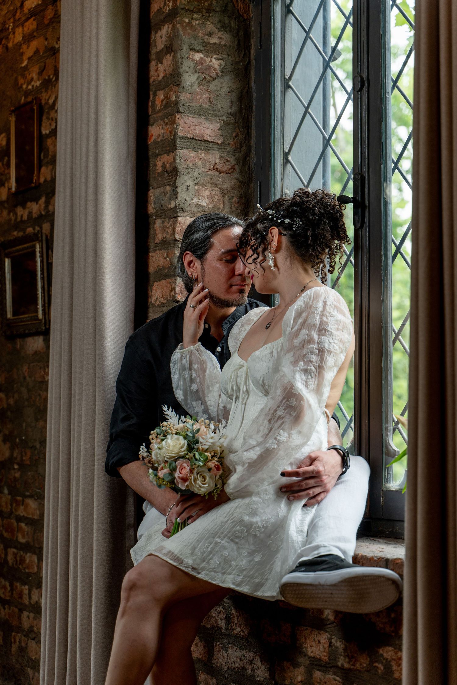 Intimate wedding portrait by a vintage window with exposed brick walls.