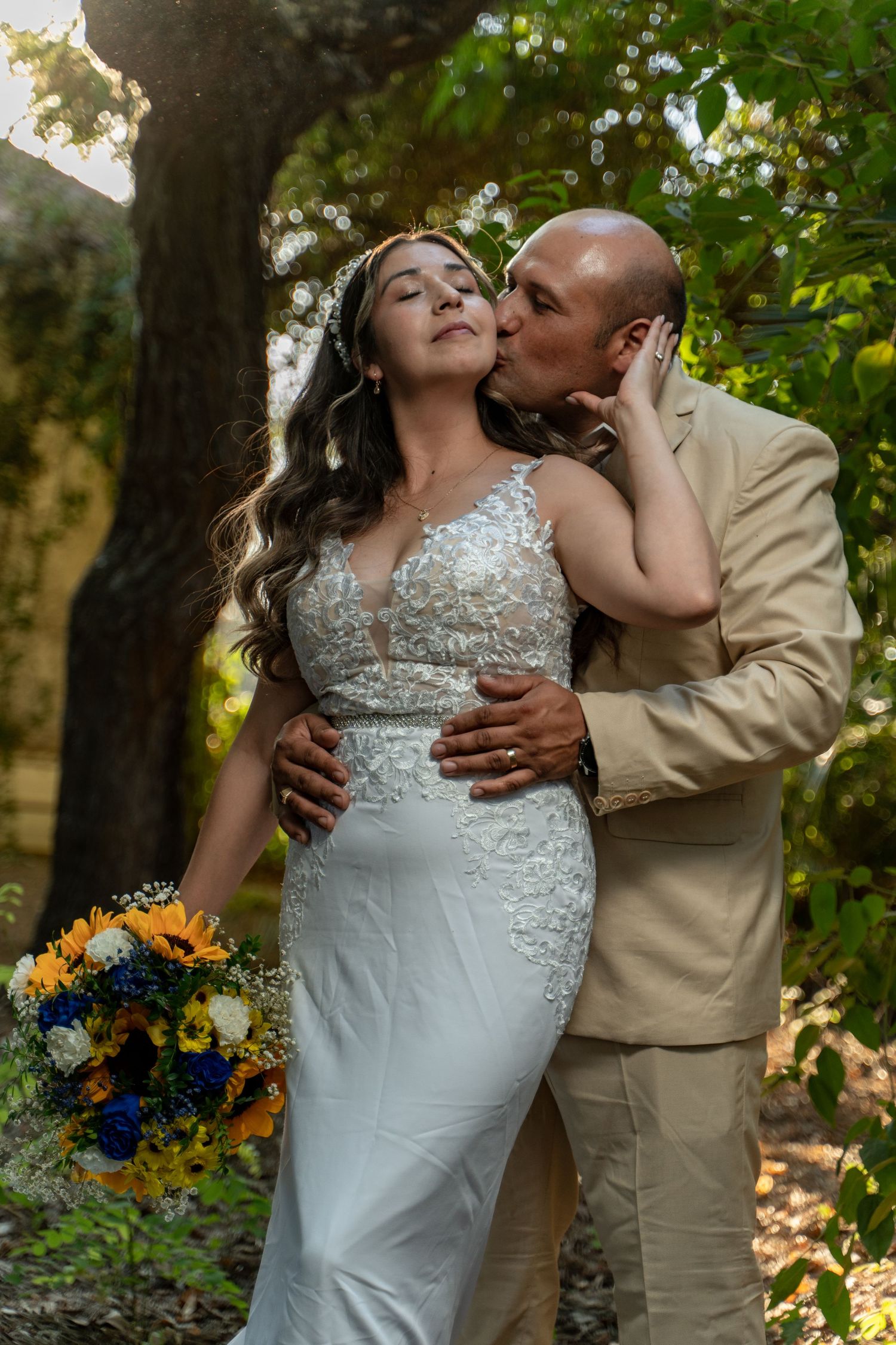 Romantic wedding couple embraces in a lush garden setting with sunflowers and natural greenery.