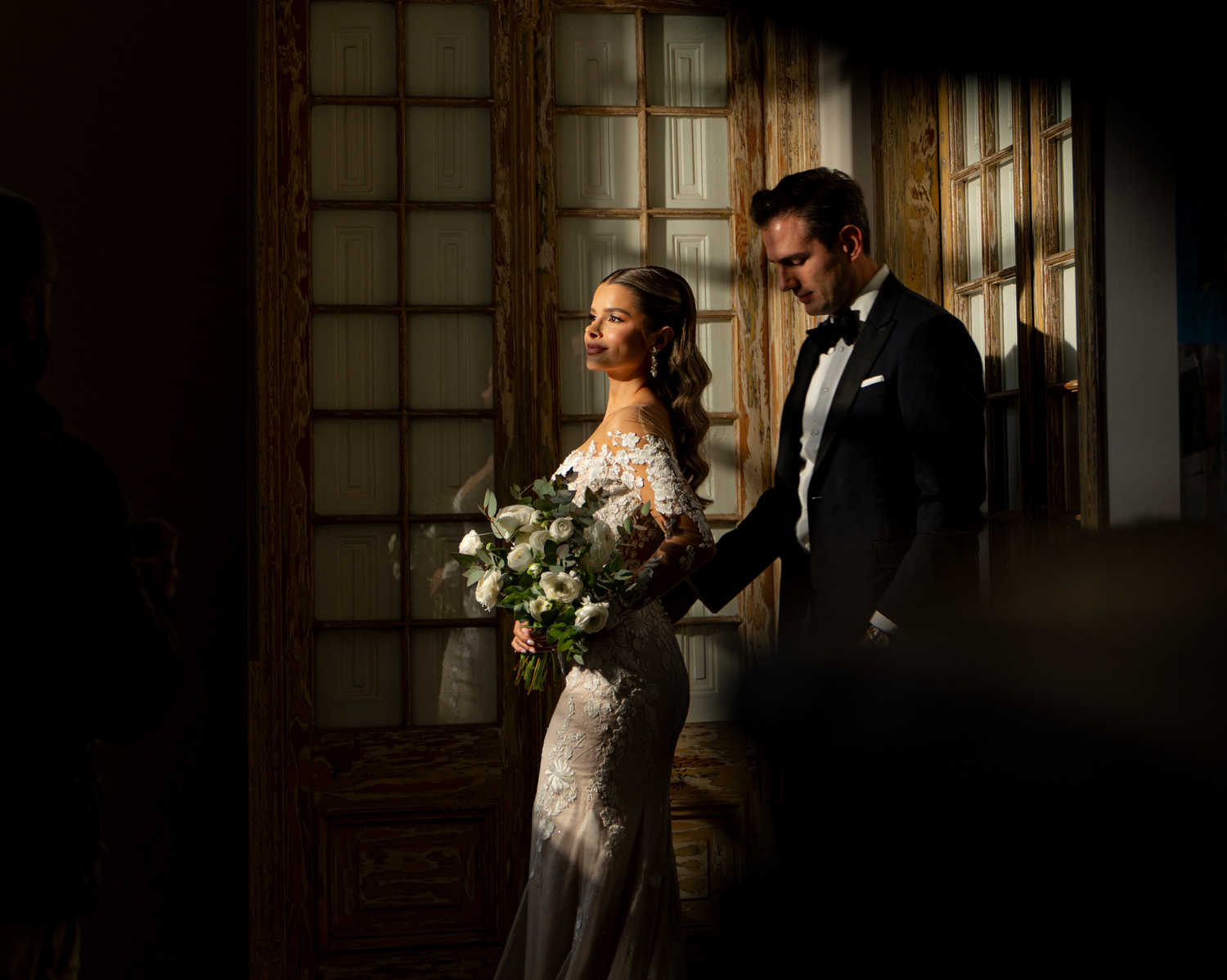 Dramatic window lighting illuminates couple in formal attire.
