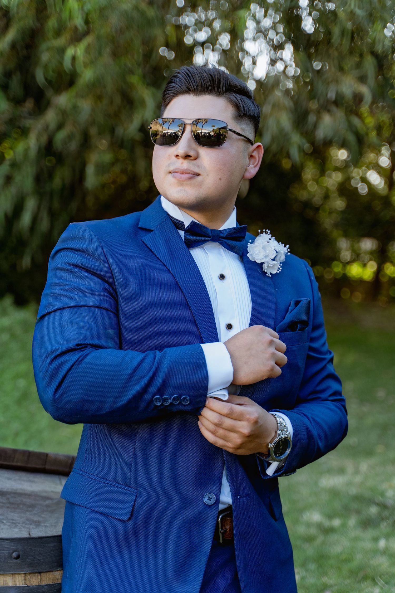 Person in a royal blue tuxedo adjusts their cuffs and boutonniere outdoors.
