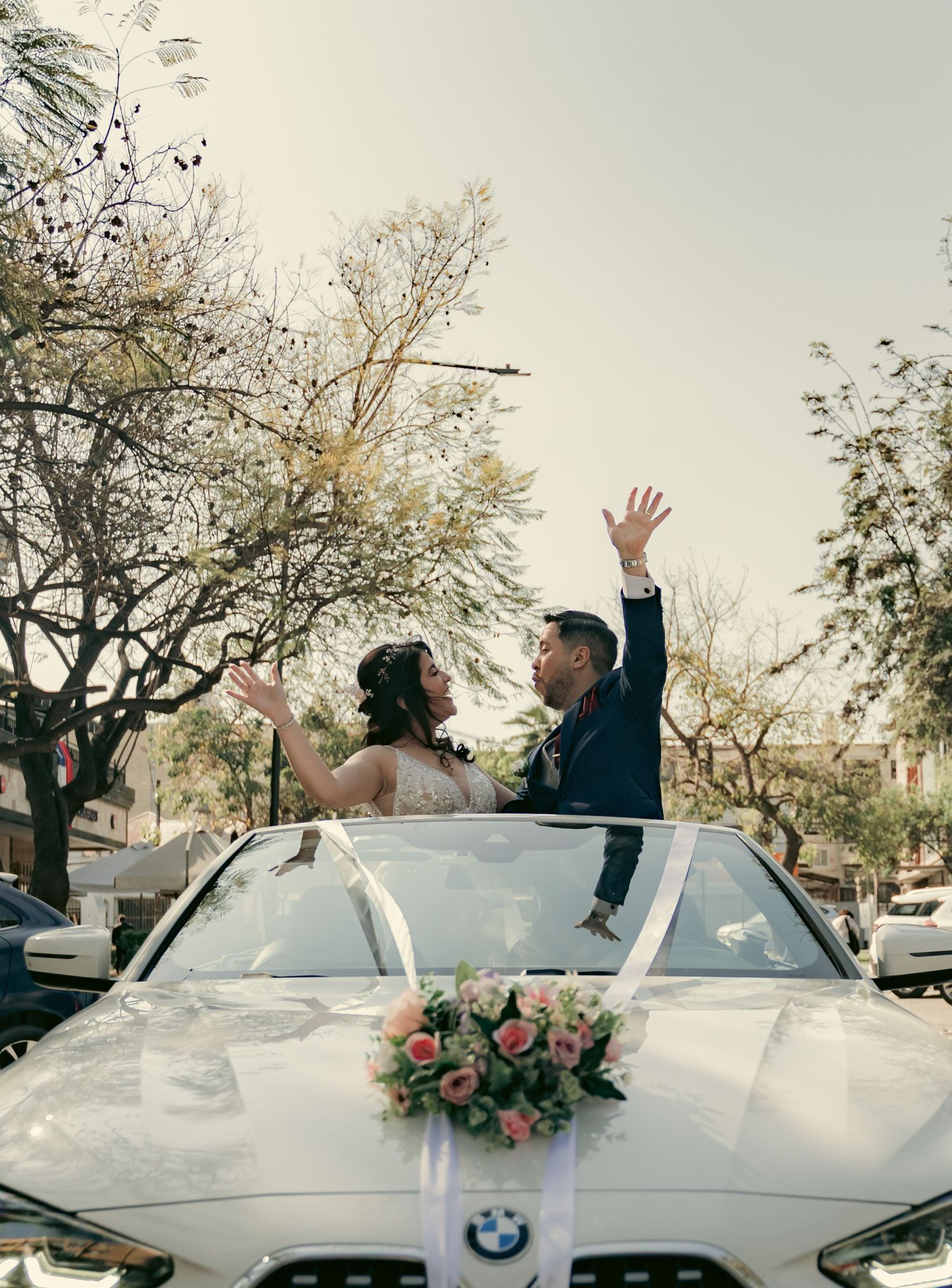 Newlyweds celebrating in a white convertible car with floral decorations.