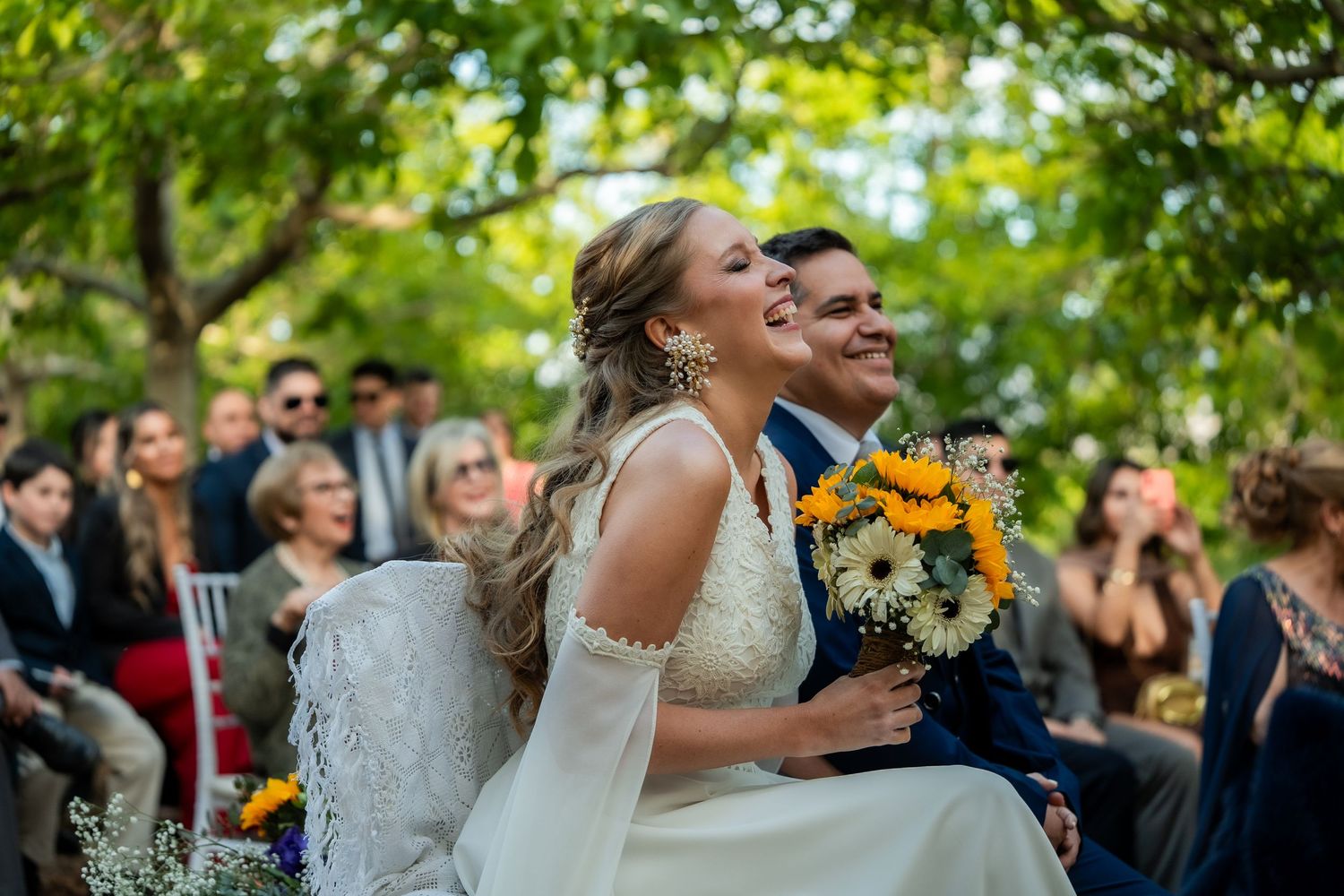 Couple shares a joyful moment during outdoor wedding ceremony with sunflowers and guests in attendance.