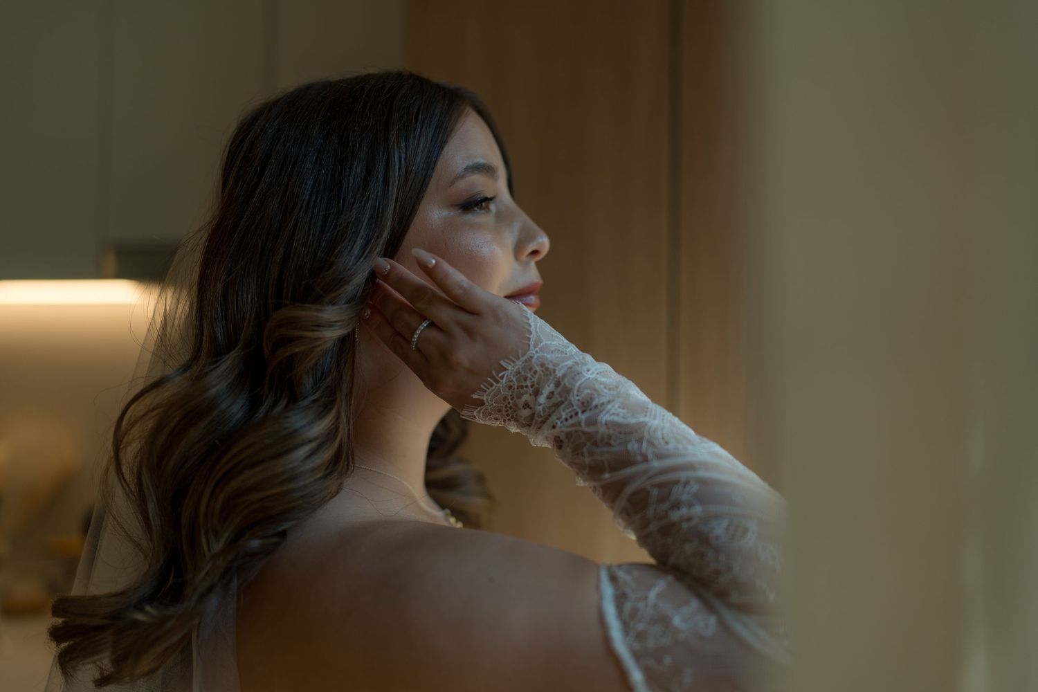 Bride in lace gloves touching her face, soft warm lighting in elegant bridal portrait.