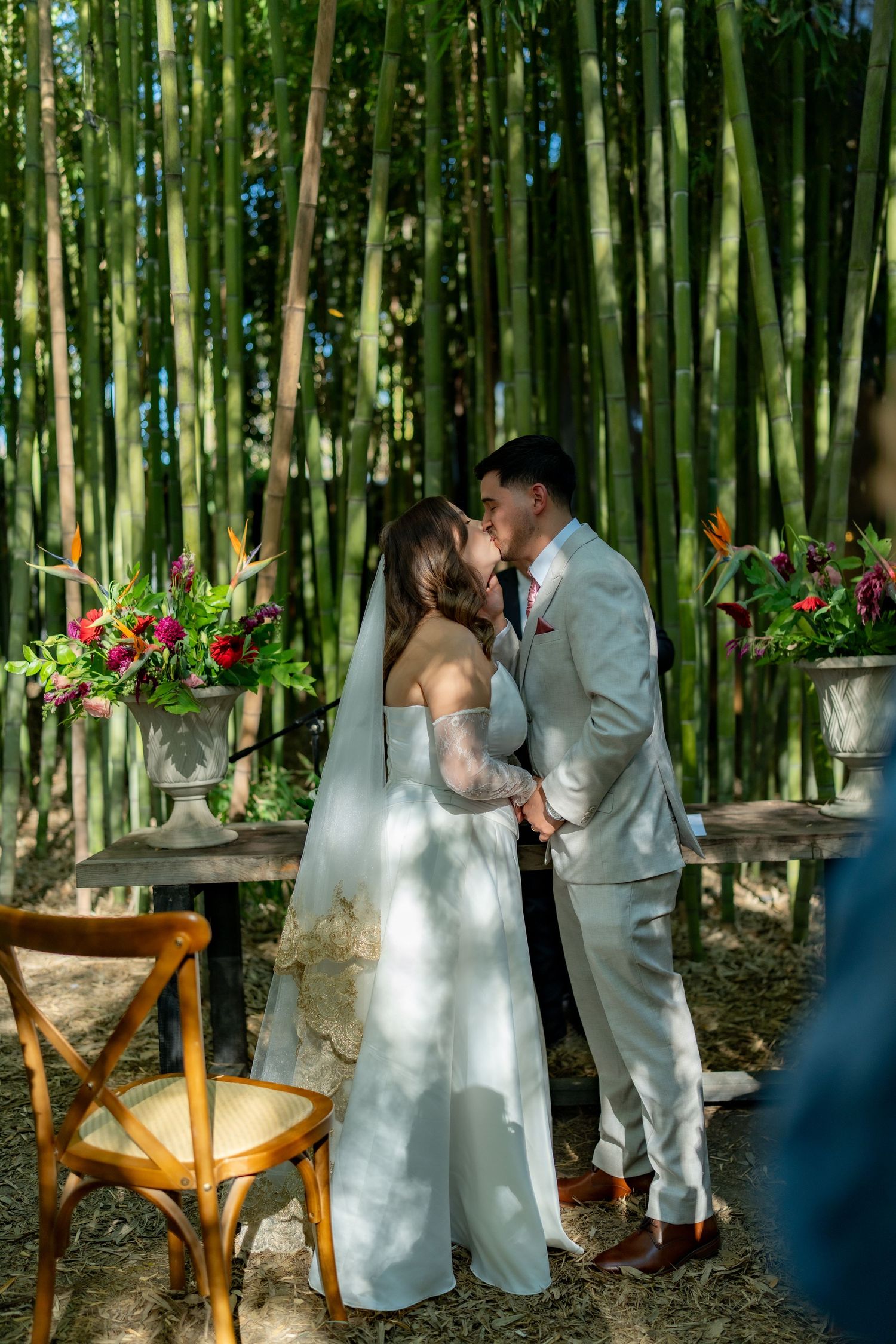 Bride and groom share their first kiss at an outdoor wedding ceremony surrounded by tall bamboo.