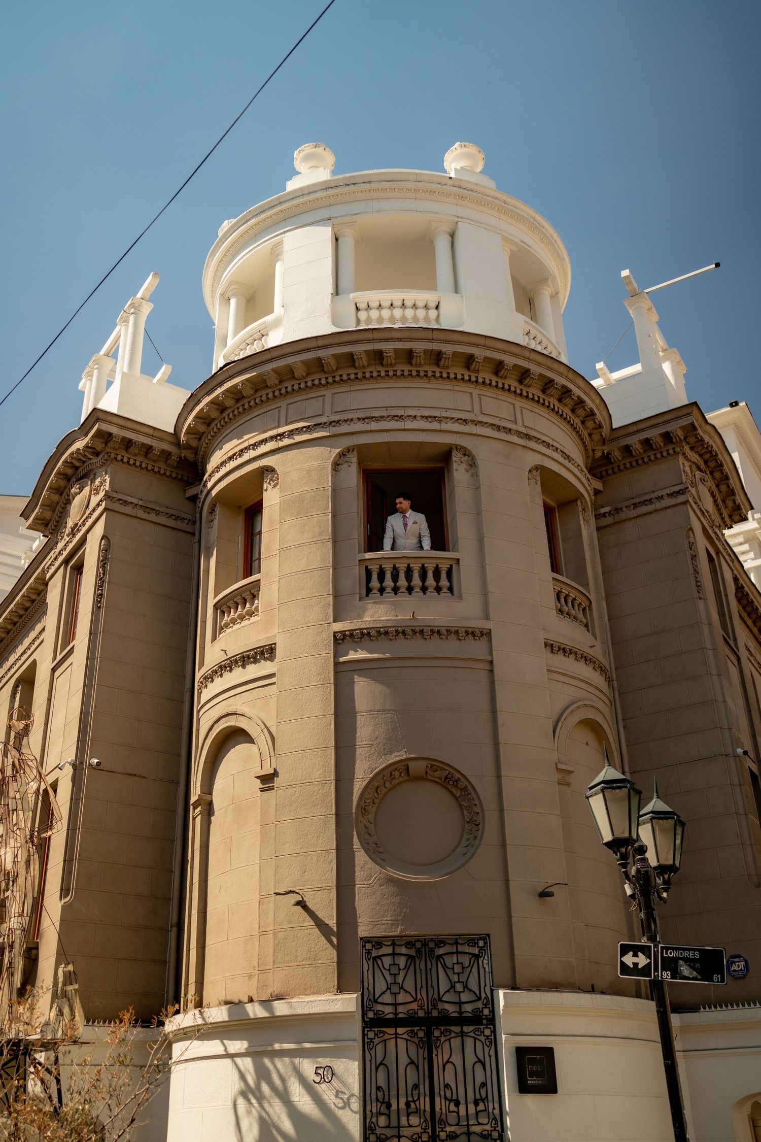 A man stands on a balcony of an ornate historic building with a cylindrical tower and classical architectural details.