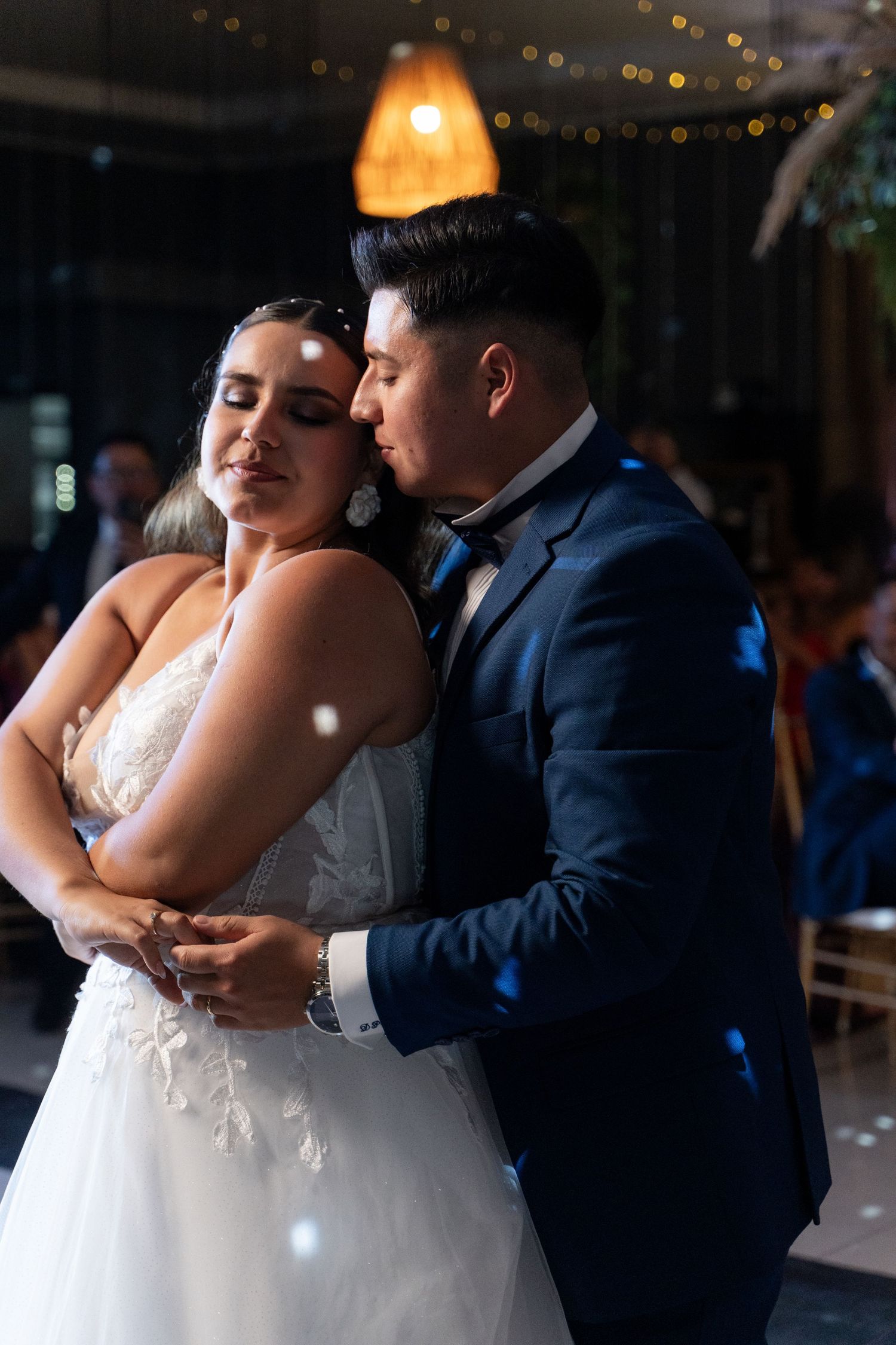 Couple shares their first dance under warm indoor lighting at wedding reception.