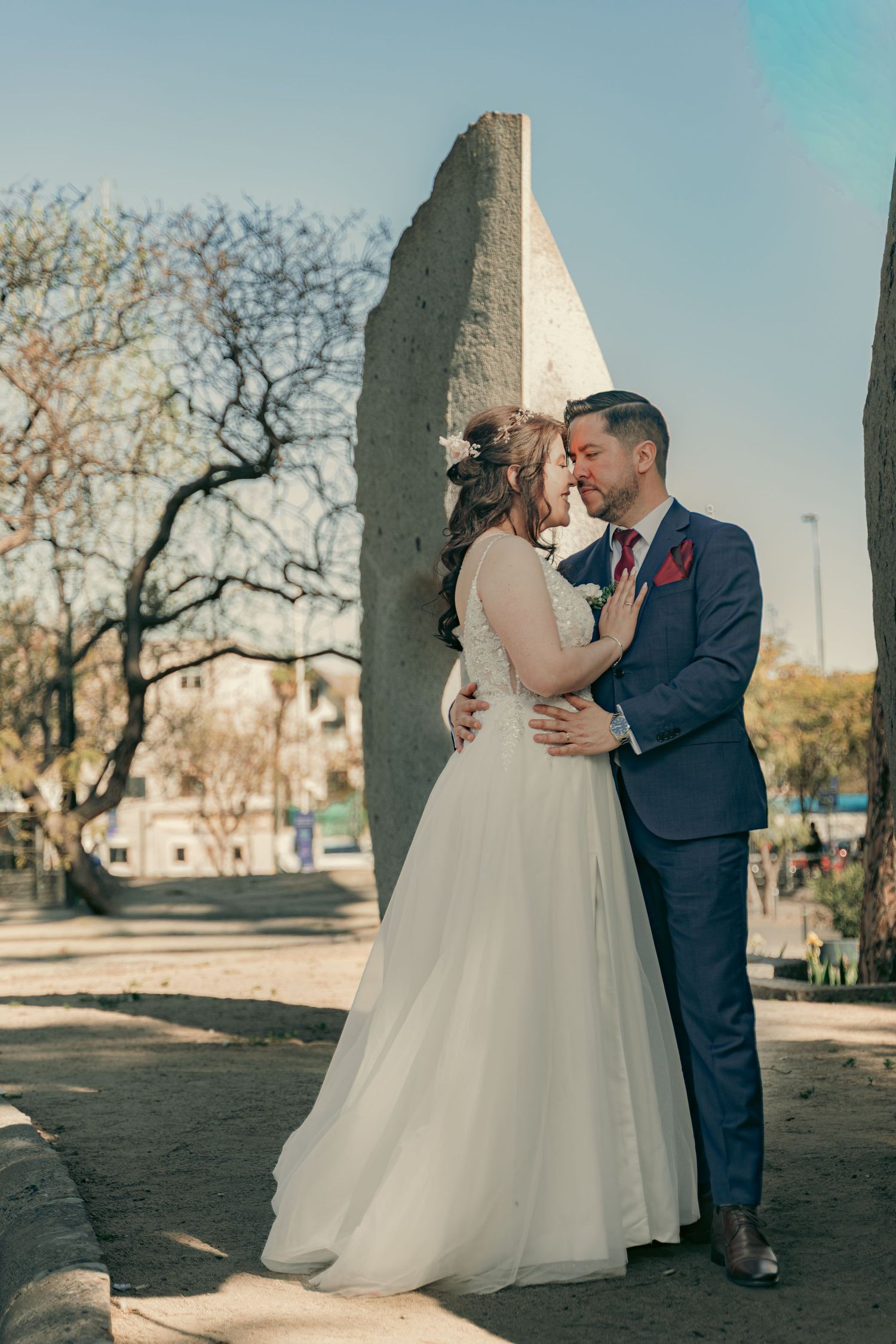 Romantic outdoor wedding portraits against stone pillars on a sunny day.