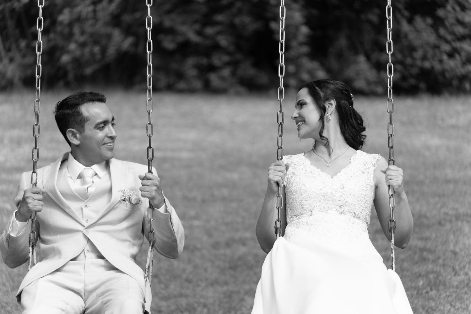 A black and white photo of a couple in wedding attire sitting on playground swings.
