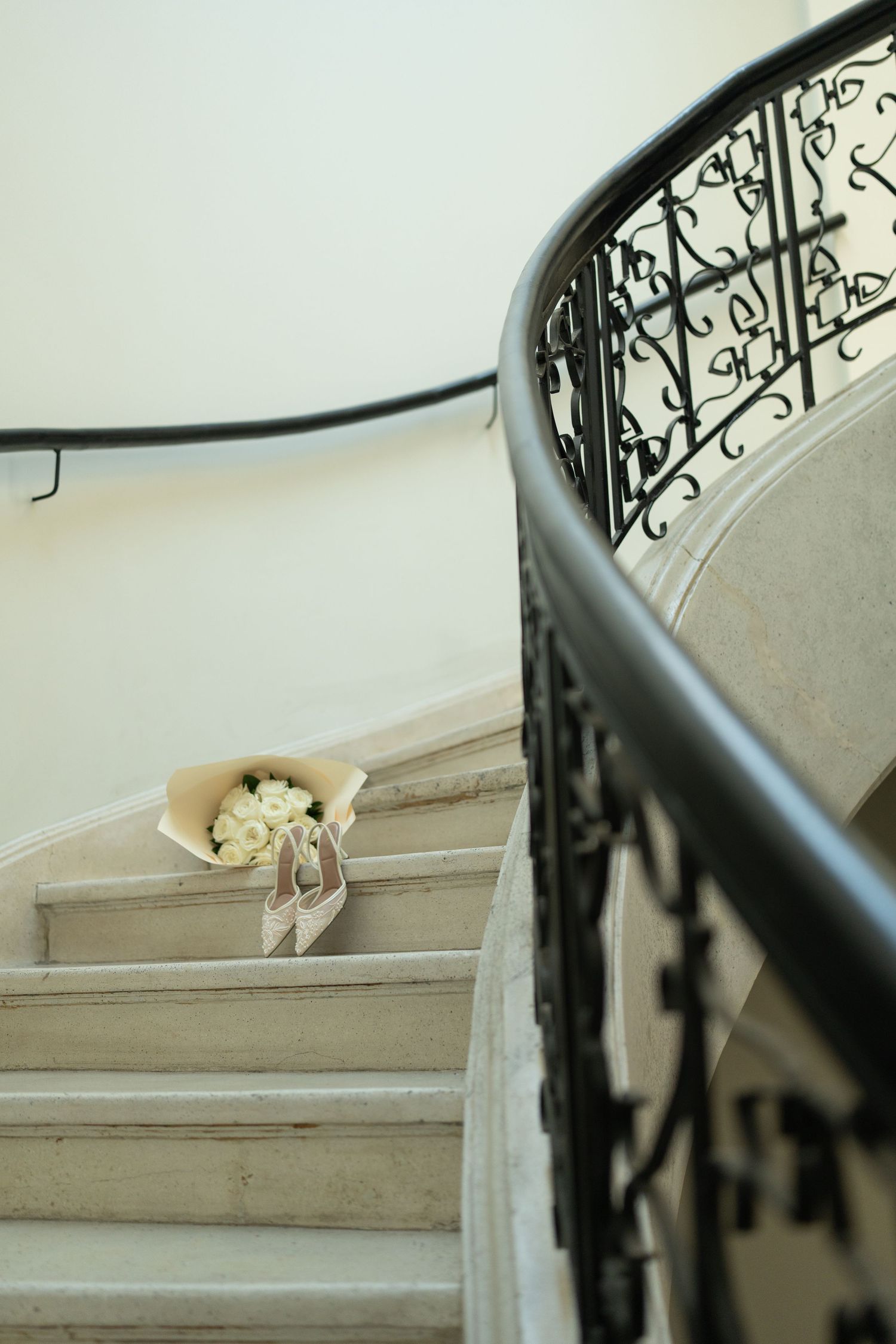 White bridal bouquet resting on elegant marble staircase with ornate black wrought iron railing.