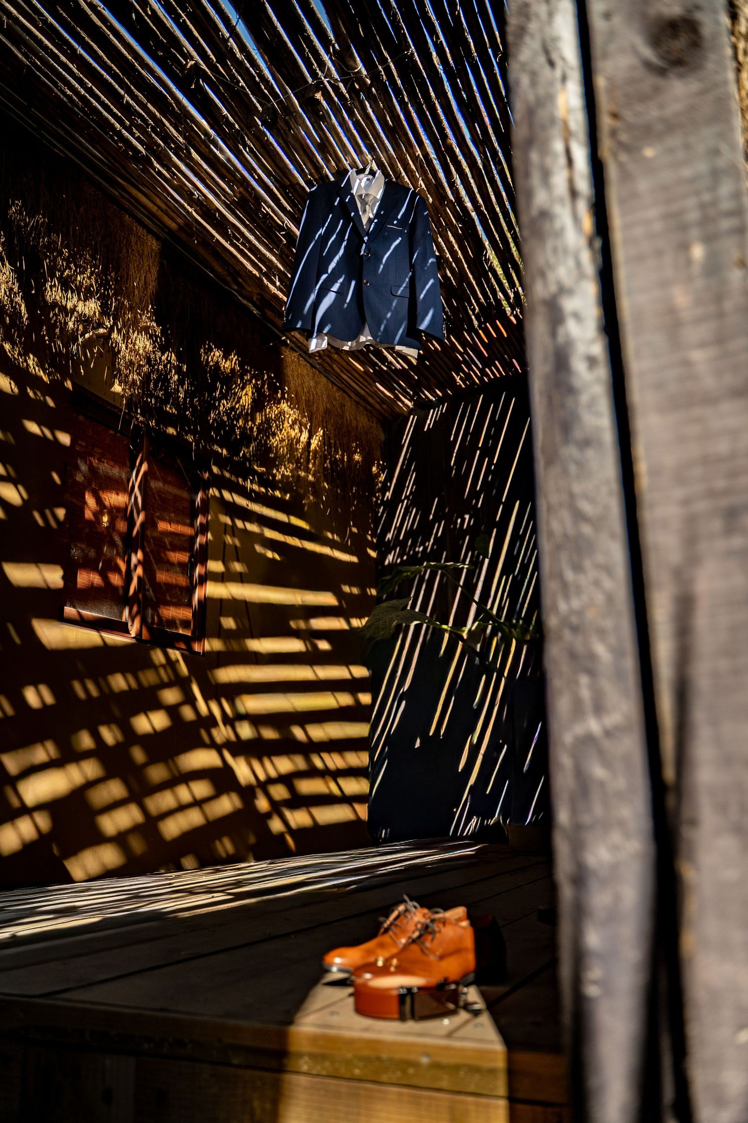 Dramatic shadows cast geometric patterns on a dark floor with brown leather shoes visible.