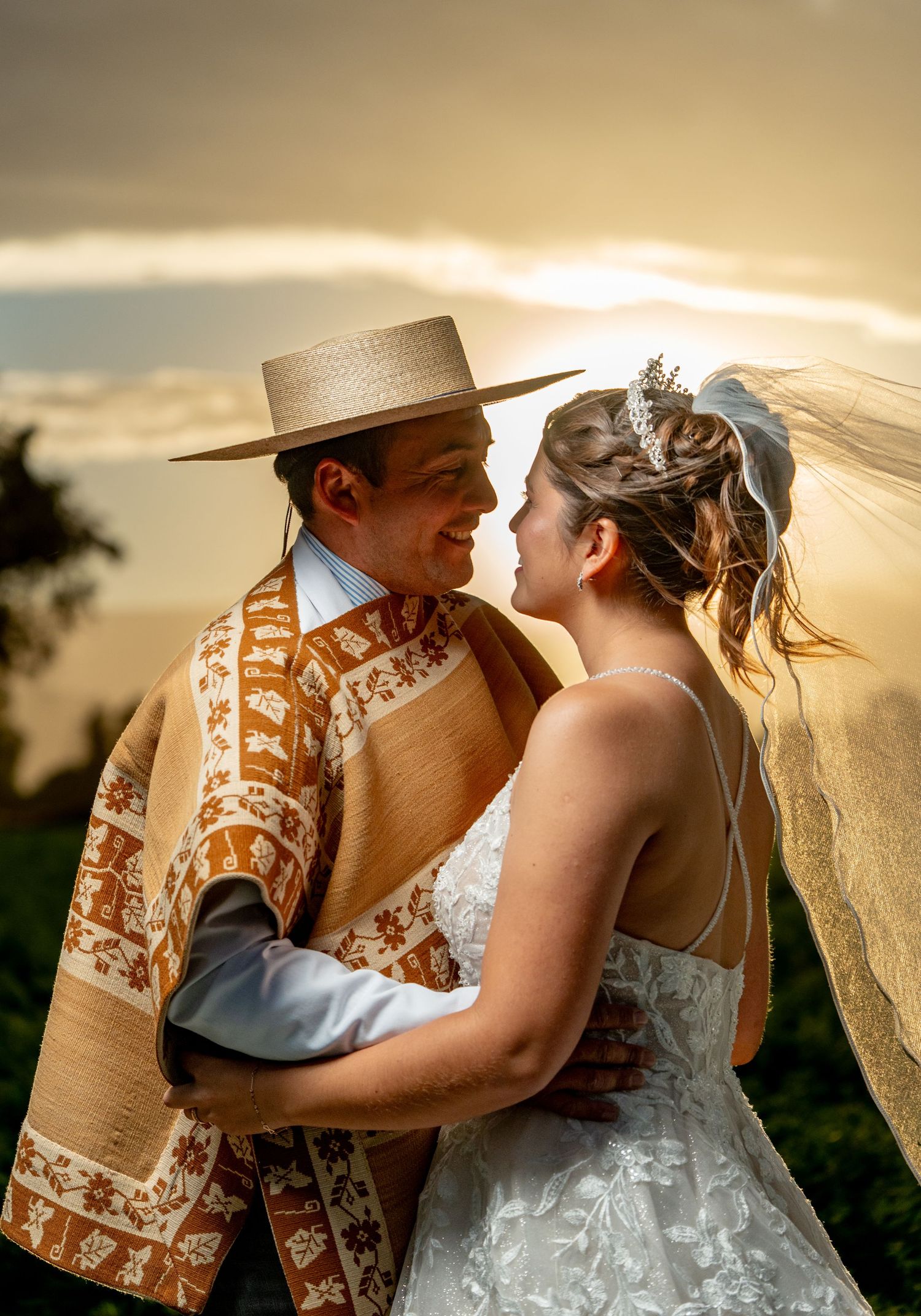 A romantic sunset wedding photoshoot with a couple in traditional Hawaiian attire and white dress embracing on a hilltop.