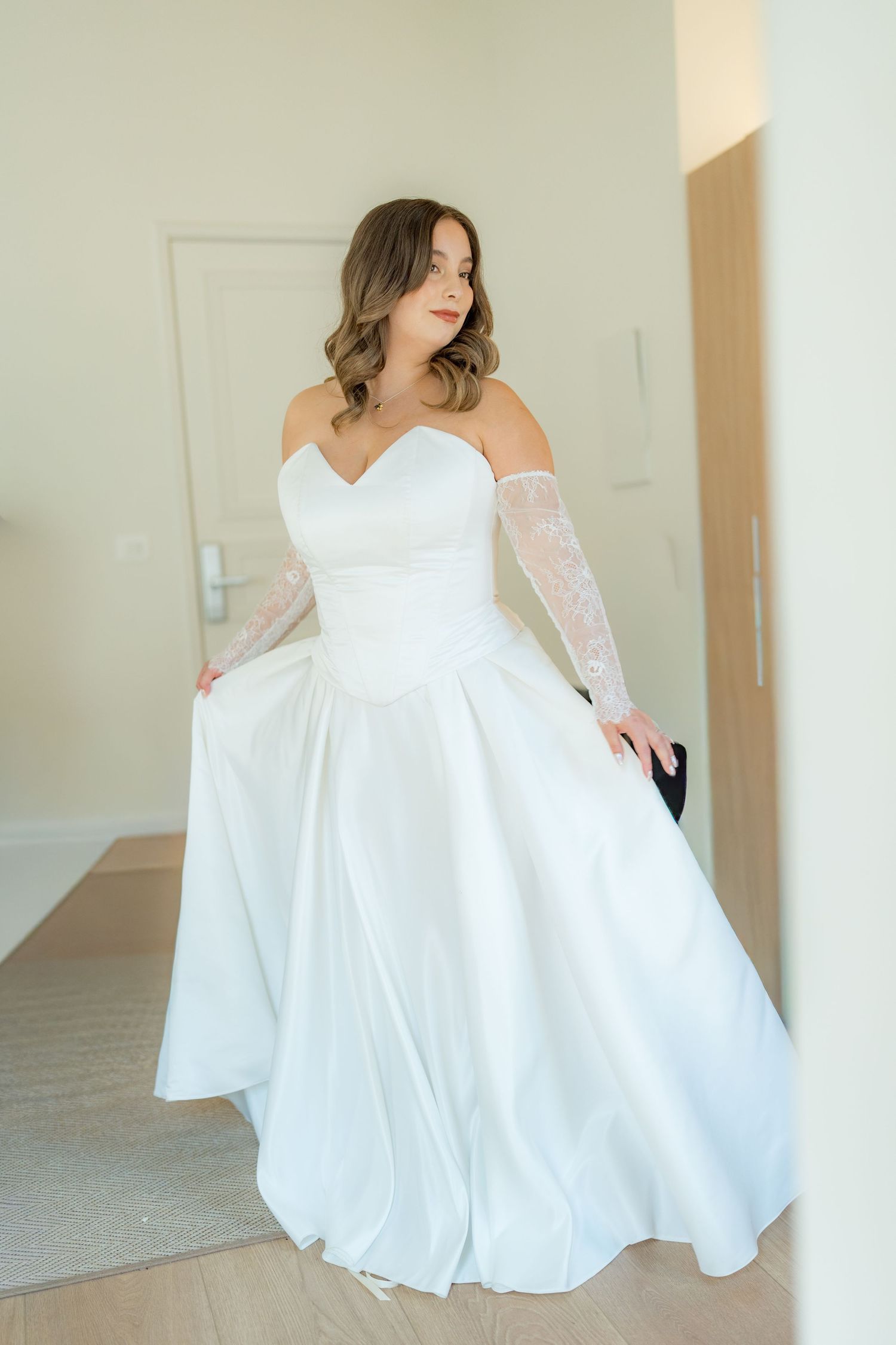 Elegant bride in a strapless white ball gown with lace gloves posing in a bright wedding suite.
