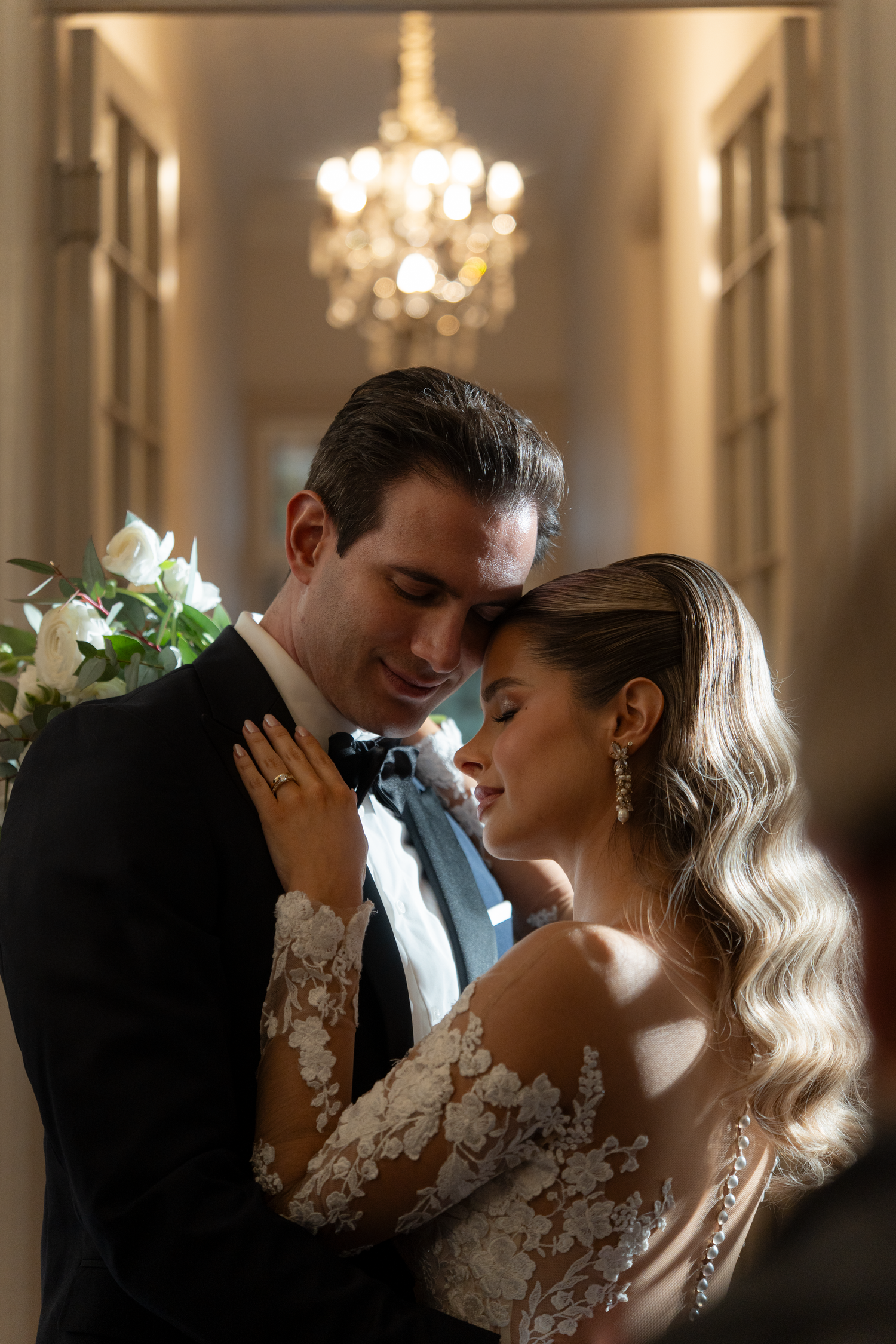 Romantic couple moment captured in elegant hallway with chandelier lighting.