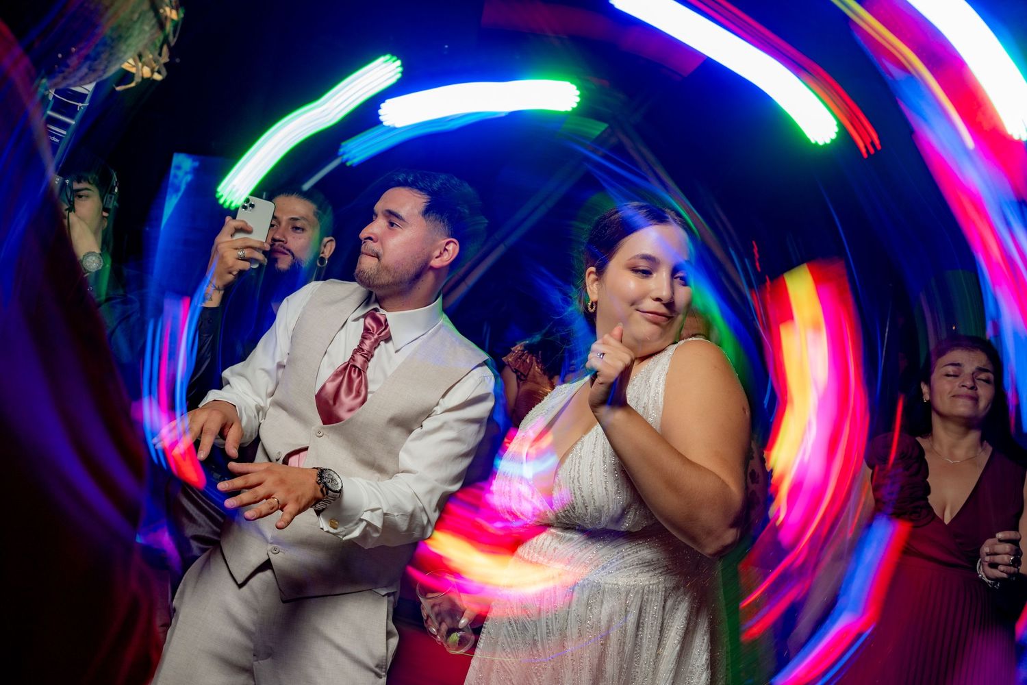 Couple dancing at a wedding reception with colorful neon light trails swirling around them on the dance floor.