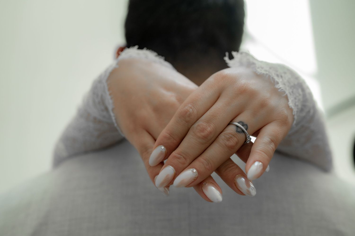 Close-up of bride's hands with white nails and diamond ring resting on groom's shoulders.