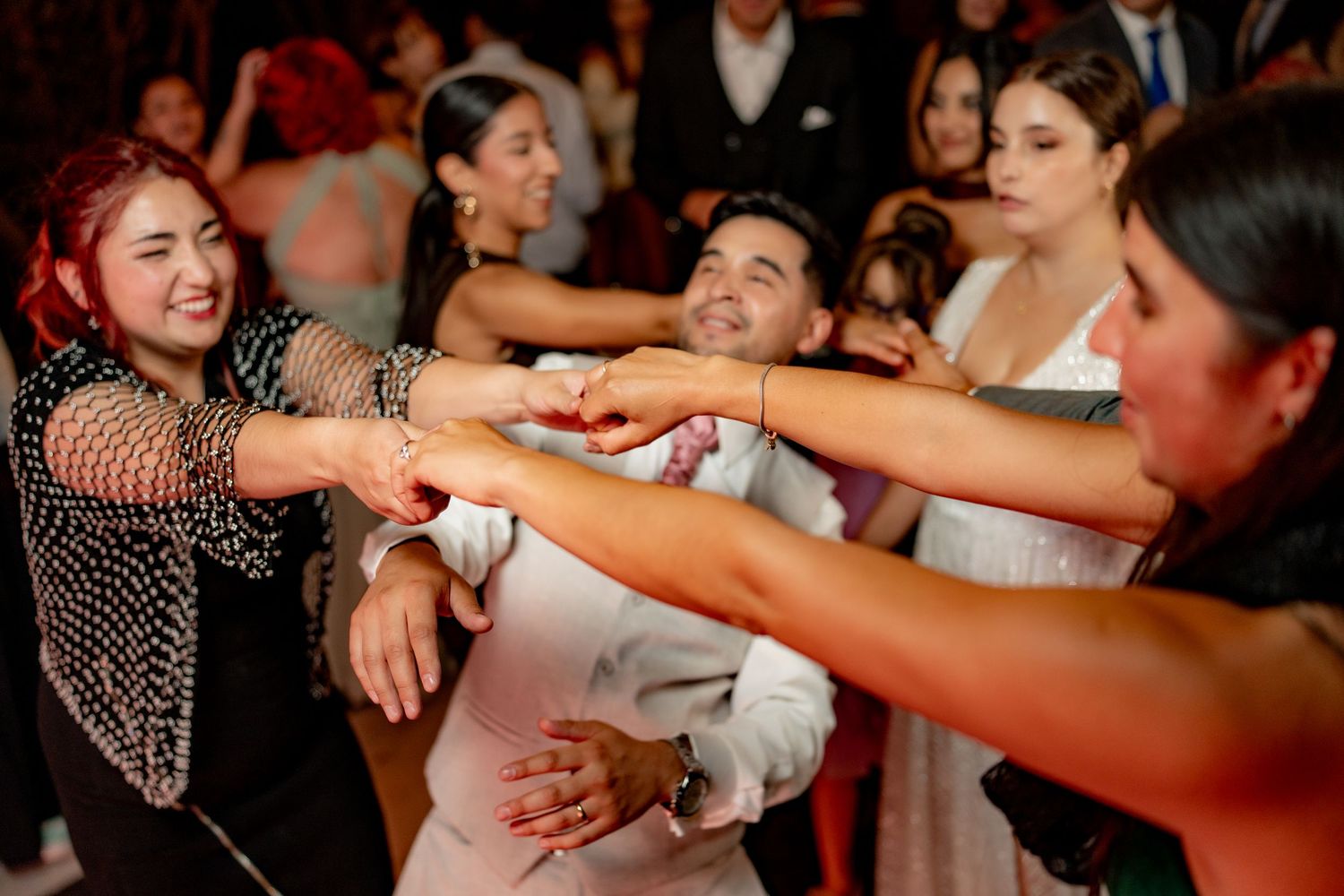 Wedding guests joyfully dancing together, reaching out hands in a lively celebration at a reception party.