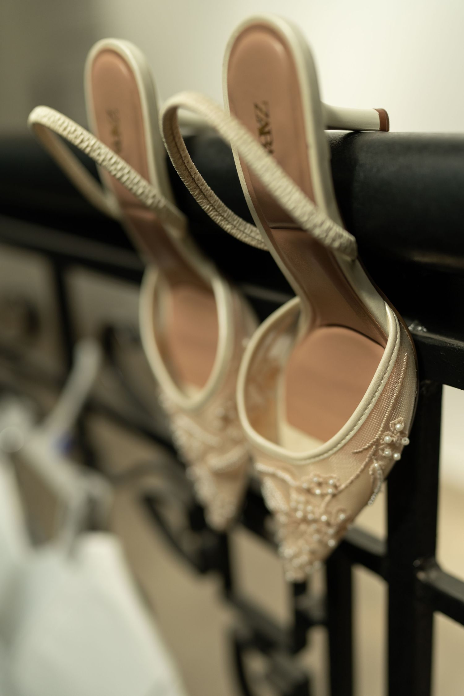 Elegant pearl-embellished bridal heels with slingback straps hanging on a black railing.