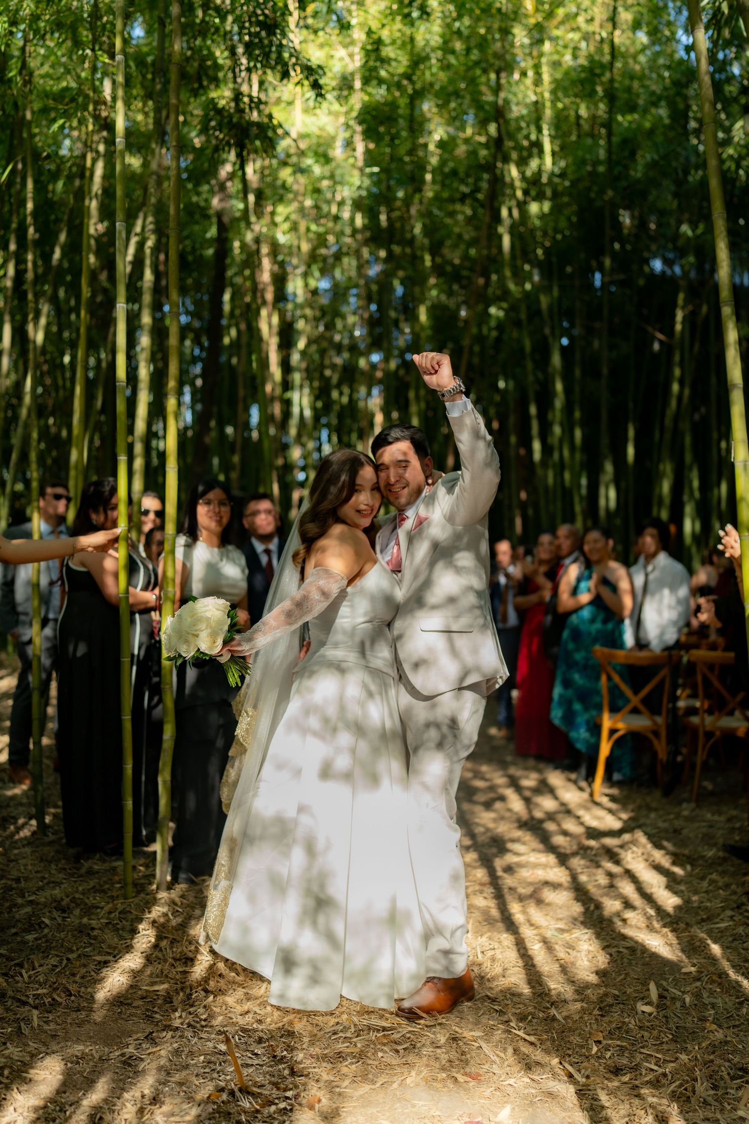 Newlyweds celebrating recessional walk through bamboo forest with cheering guests.