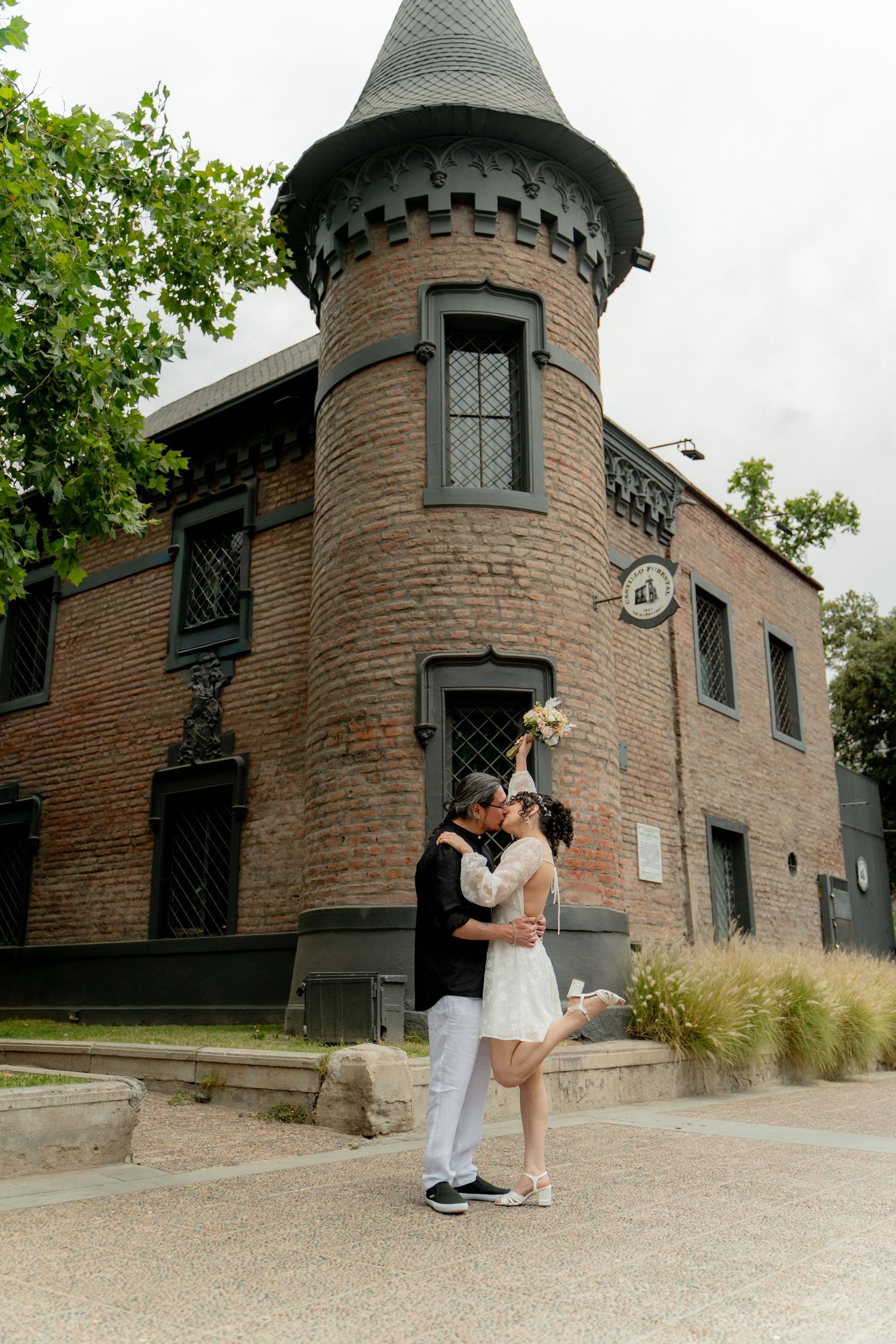 Couple embracing outside a historic brick building with a turret.