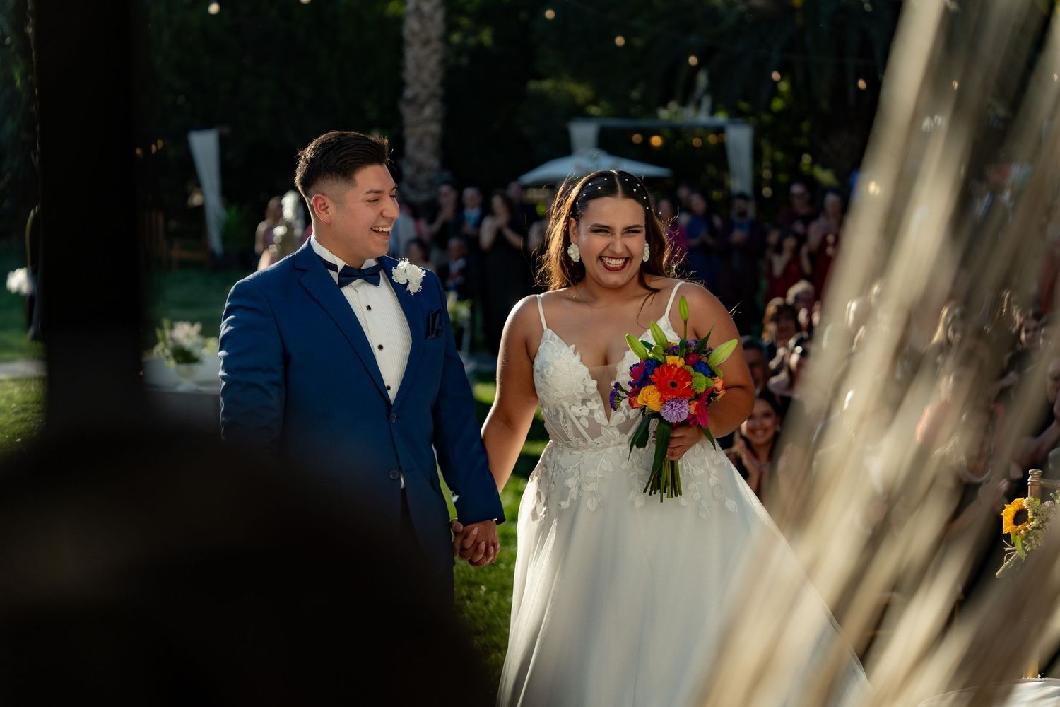 Wedding couple walks down a tree-lined path surrounded by guests holding sparklers during an evening celebration.
