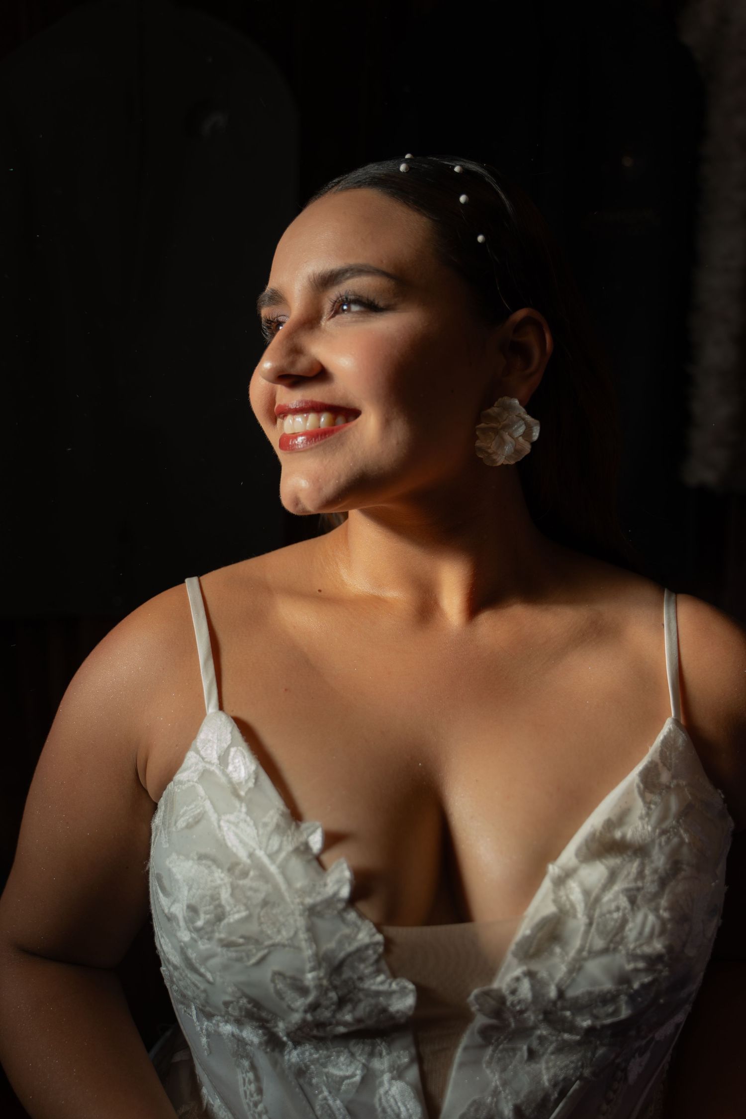 Dramatic side-lit portrait showcasing intricate details of a white lace wedding gown.