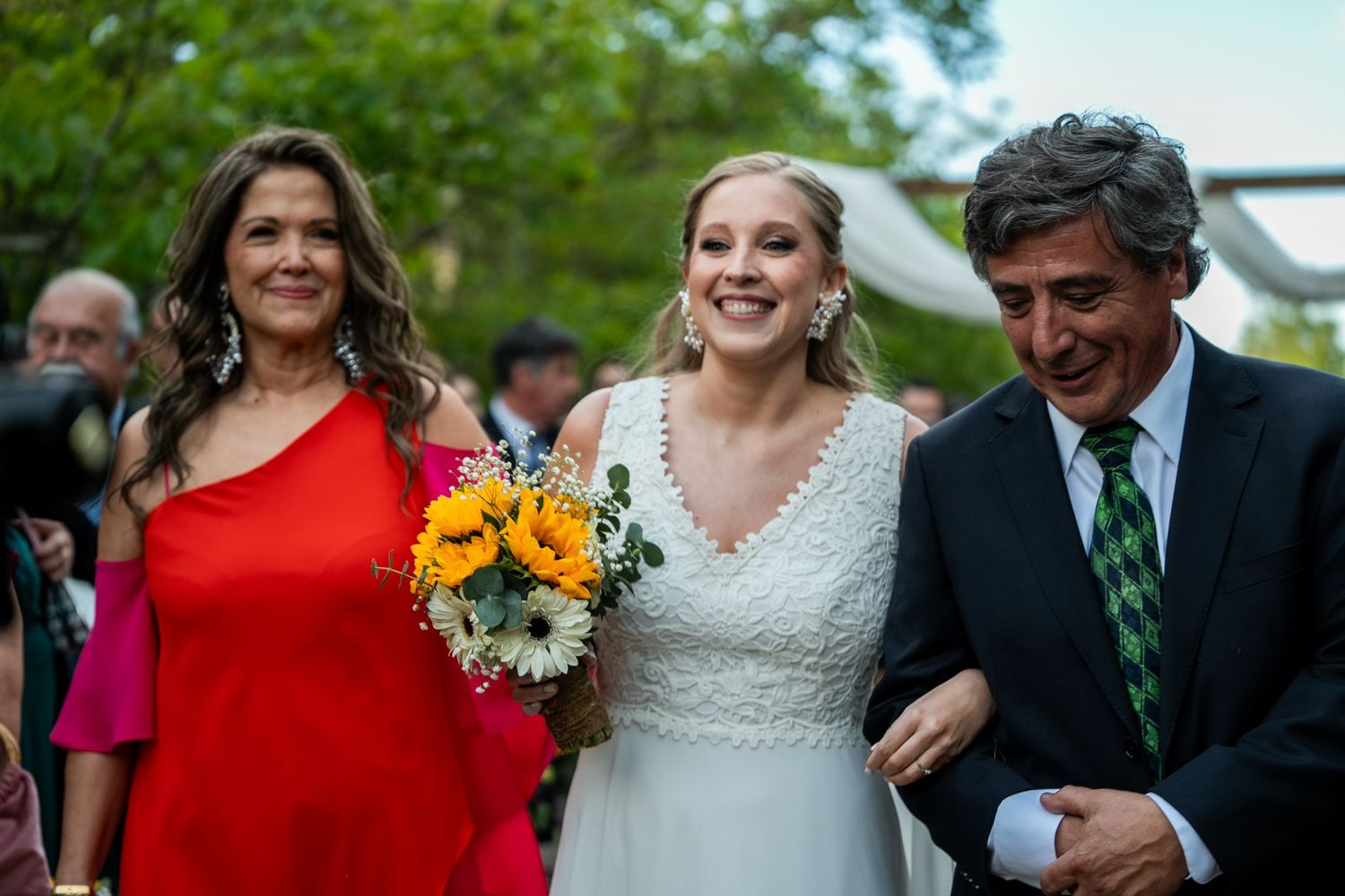 Wedding party walking outdoors with bright red dresses and sunflower bouquets.