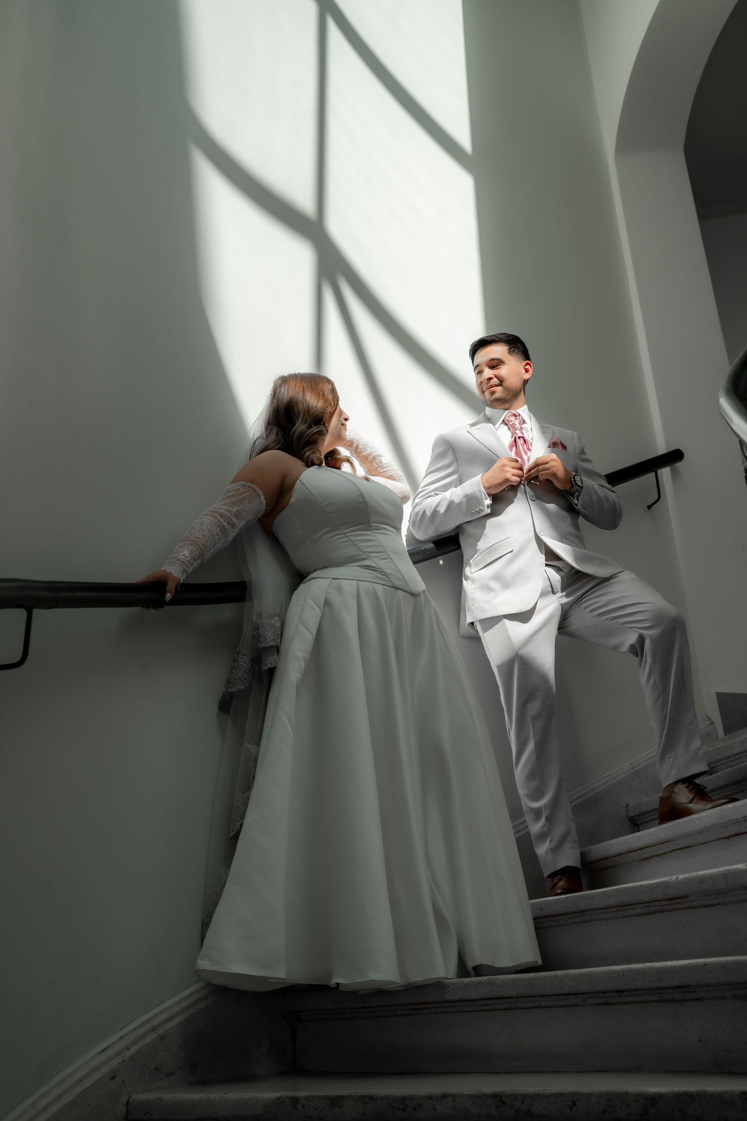 Bride and groom sharing a romantic moment on sunlit staircase.