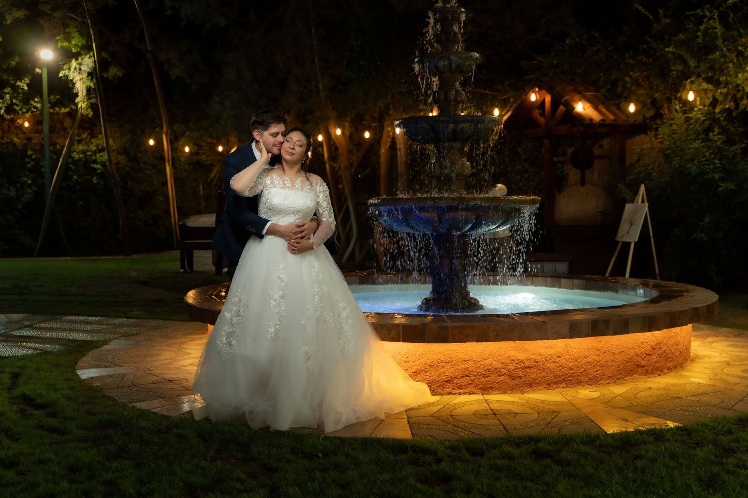 Romantic nighttime wedding photos captured in a garden setting with illuminated fountains and pathways.