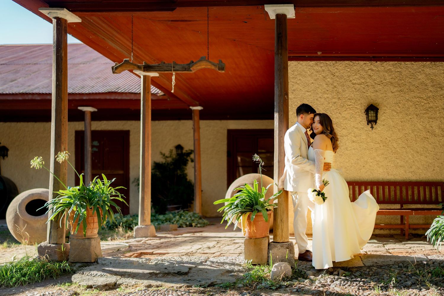Bride and groom share a romantic moment outside a rustic venue surrounded by lush greenery and terracotta pots.