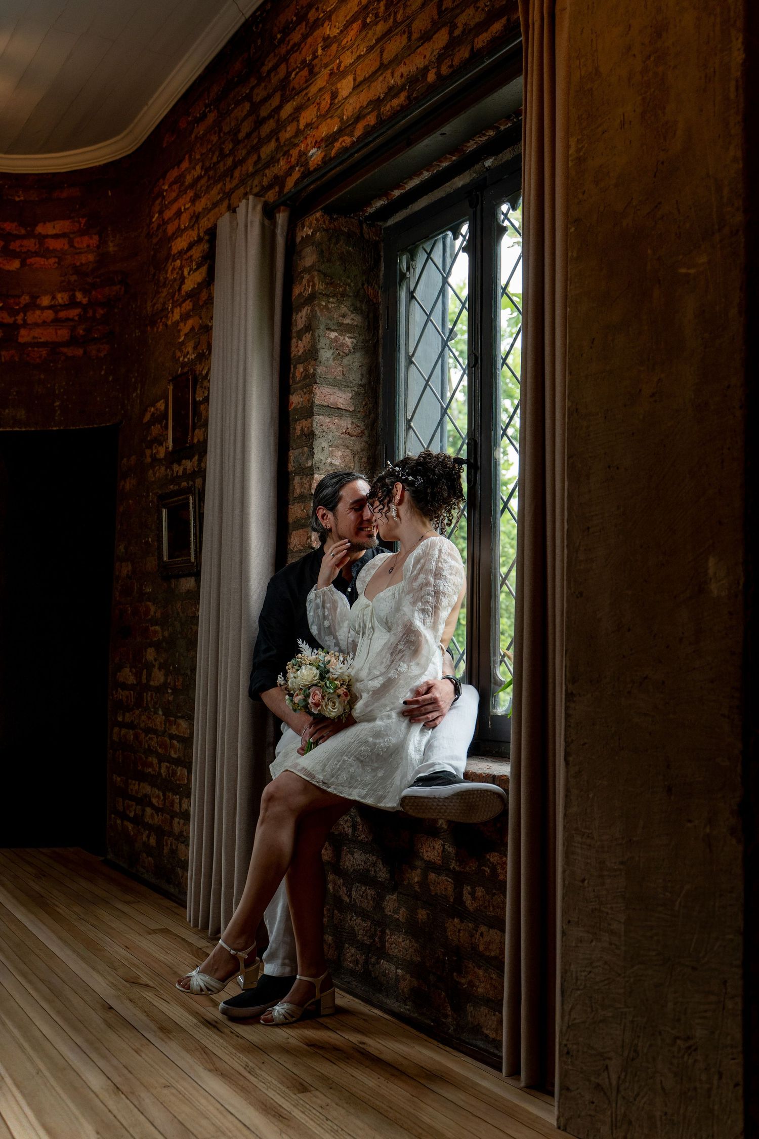 Couple sharing intimate moment by window in rustic brick interior.