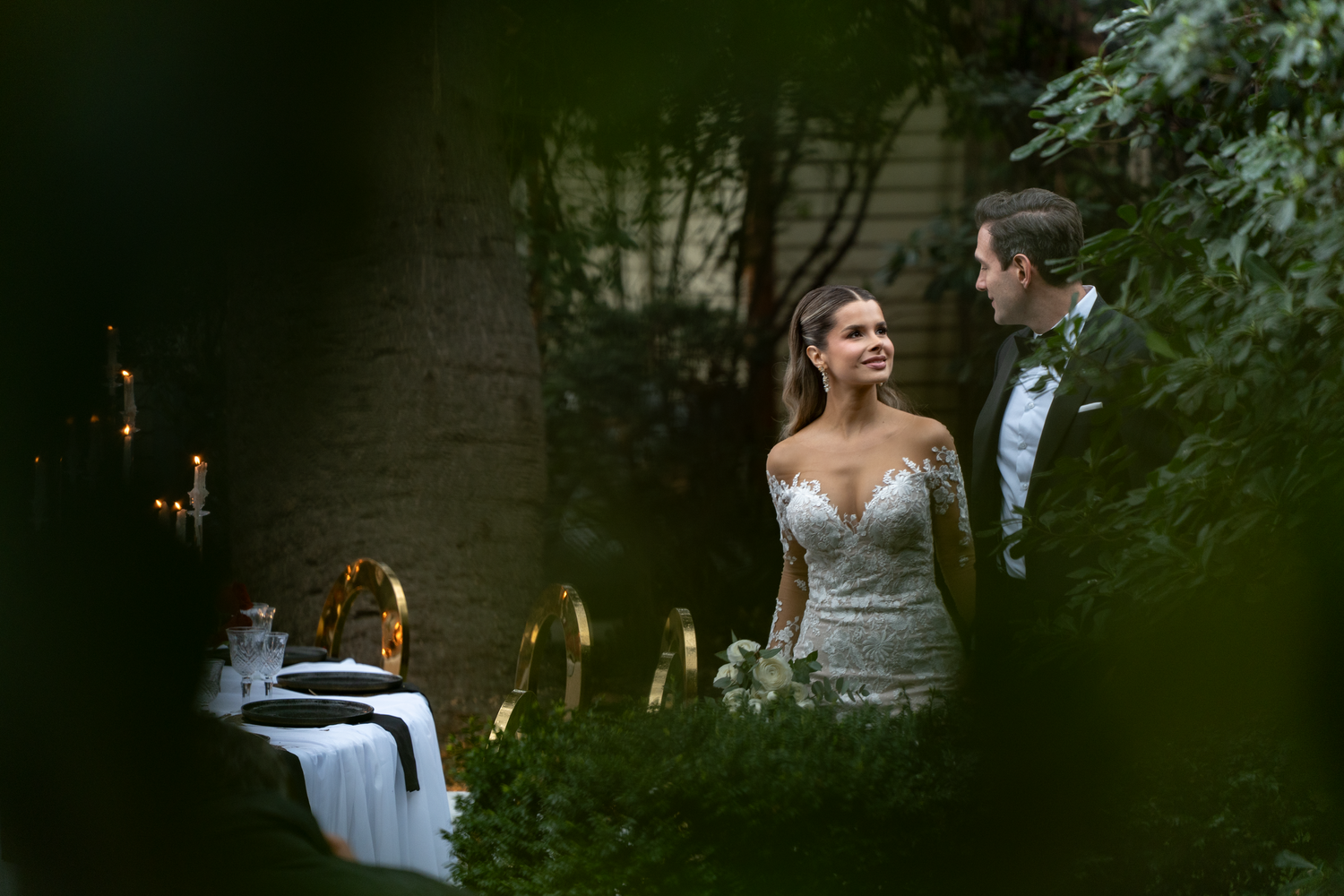 Newlyweds share tender moments against a lush garden backdrop at dusk.