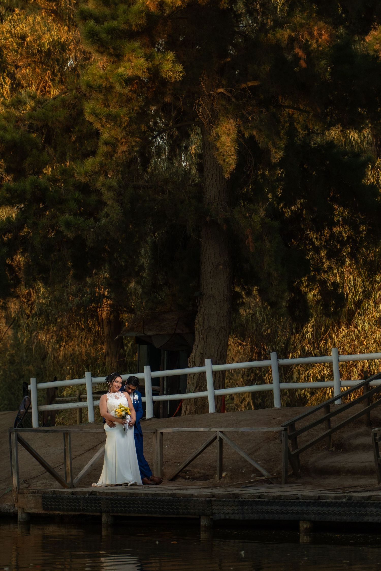 Wedding couple poses romantically on a wooden dock during golden sunset.