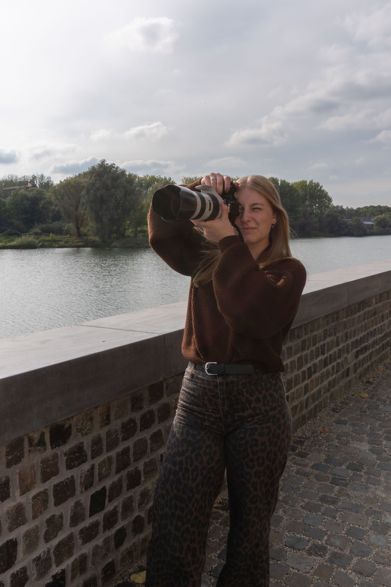 Young woman photographing with professional camera on historic brick bridge by river.