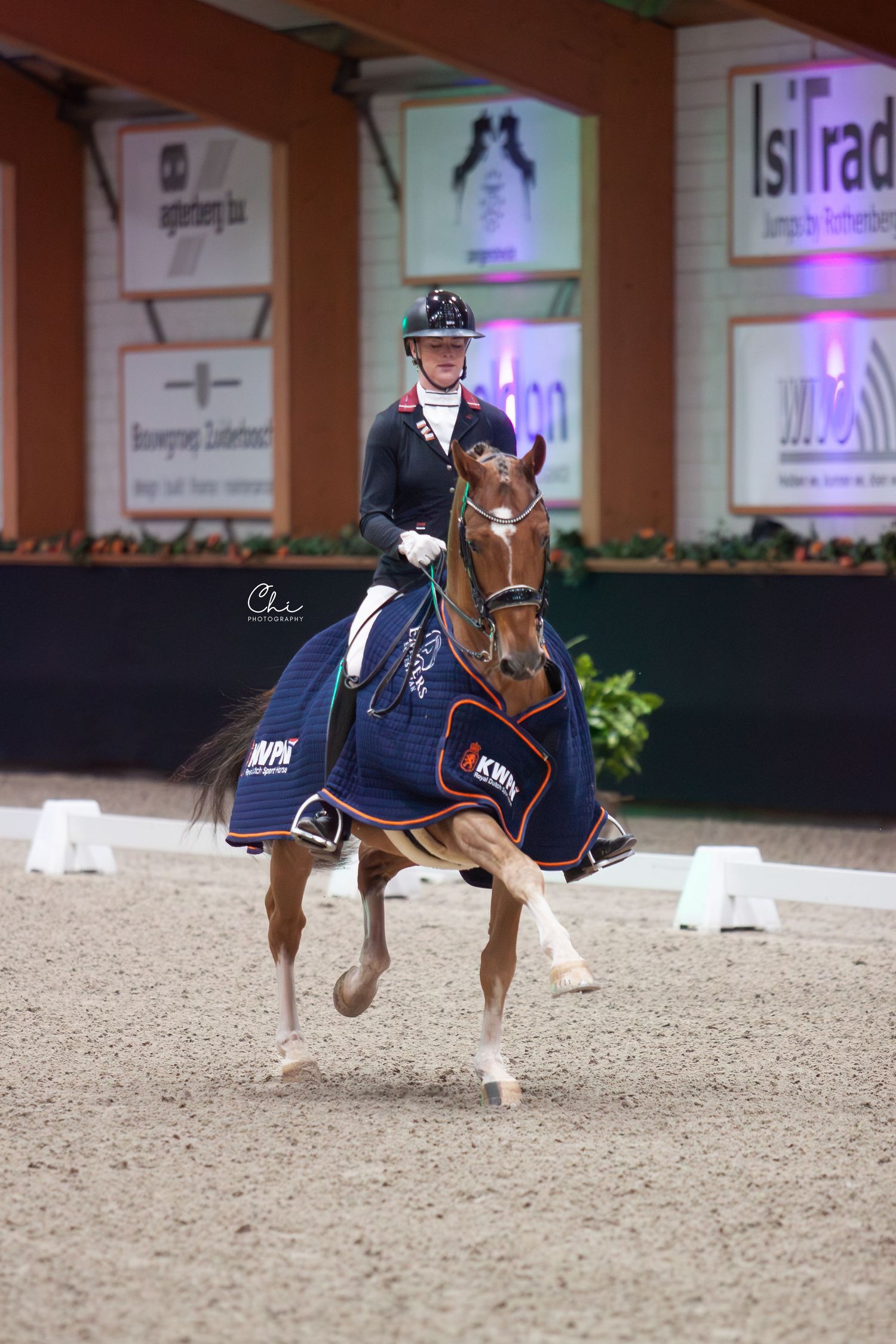 A rider on a decorated chestnut horse performs dressage in an  indoor equestrian competition.
