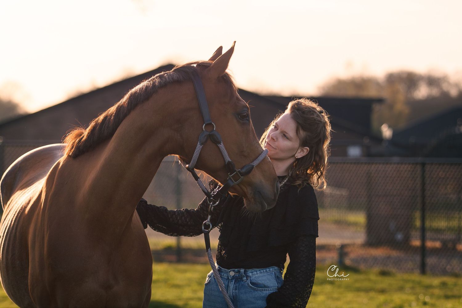 A woman in a black top shares a tender moment with a chestnut horse at golden hour sunset.
