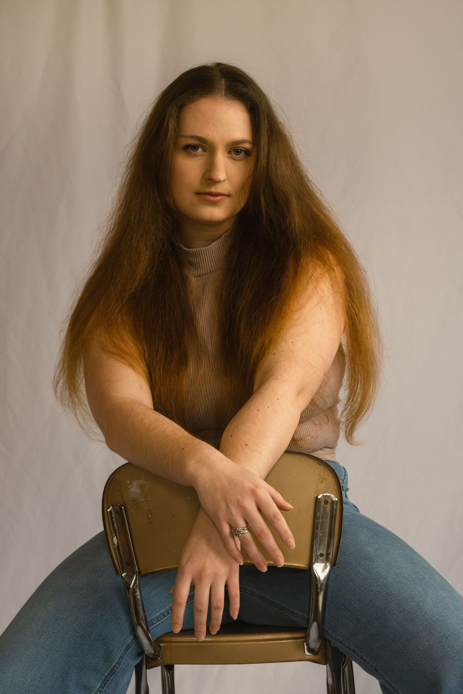 A series of artistic portrait photographs showing a person with long brown hair sitting on a wooden chair against a neutral backdrop.