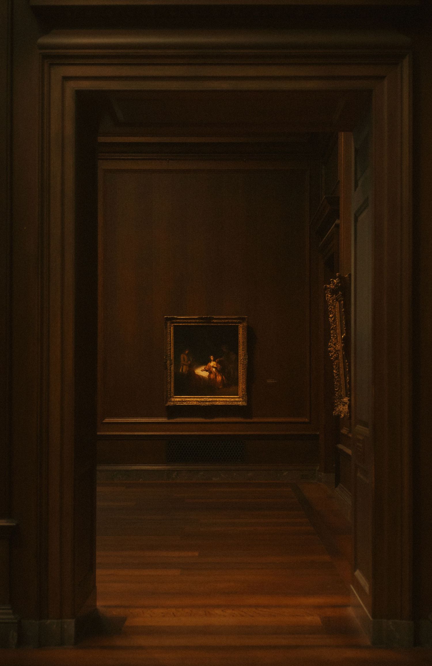 A series of dark museum hallways with wooden floors and paneled walls leading to a small illuminated painting in the distance.