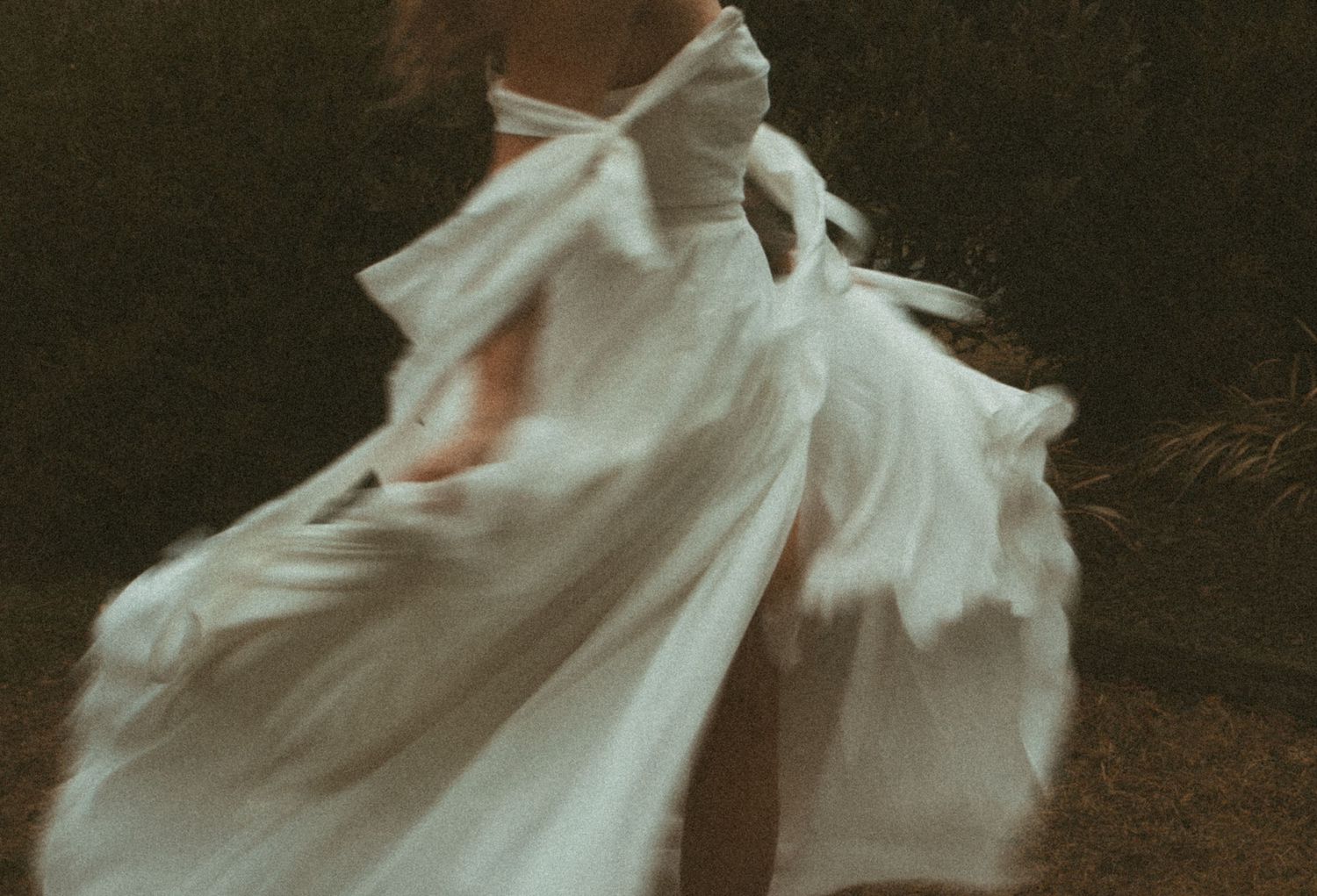 An ethereal figure in flowing white fabric dances gracefully against a dark background in a dreamy, motion-blurred photograph.