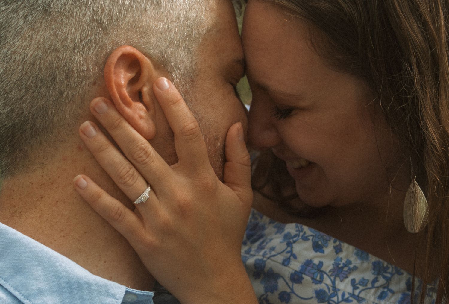 Couple sharing an intimate moment, woman wearing engagement ring gently touching mans face, smiling tenderly.