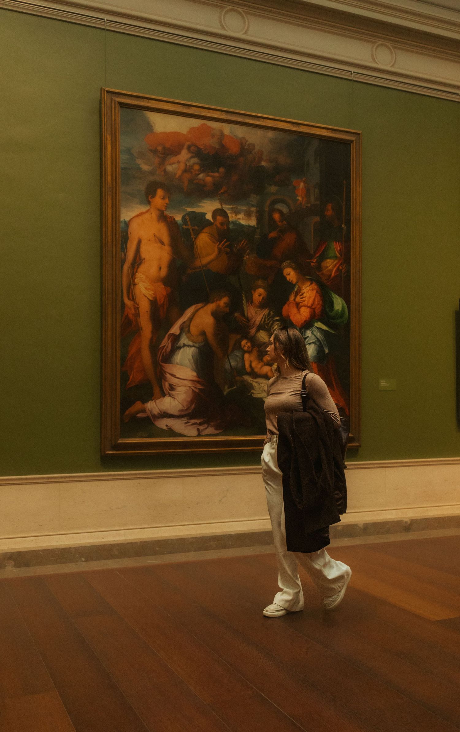 Museum visitors observe classical paintings displayed on green walls in an art gallery.