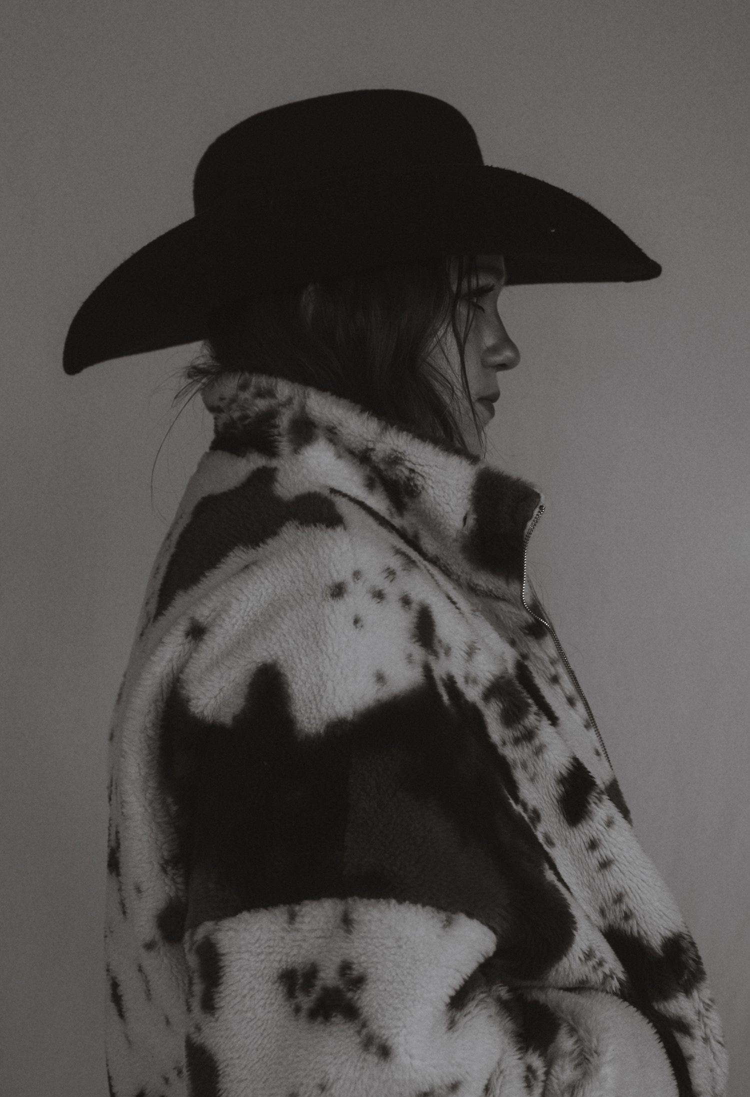 Black and white artistic portrait of a person wearing a cowboy hat and spotted pattern clothing in a dark setting.