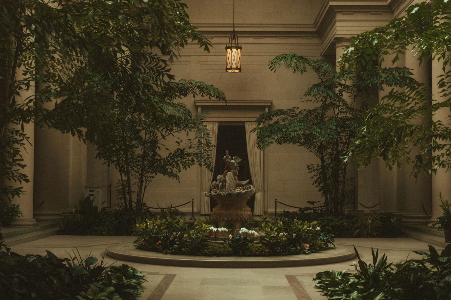 Elegant courtyard with stone fountain, archways, and lush greenery in a Mediterranean-style architectural setting.