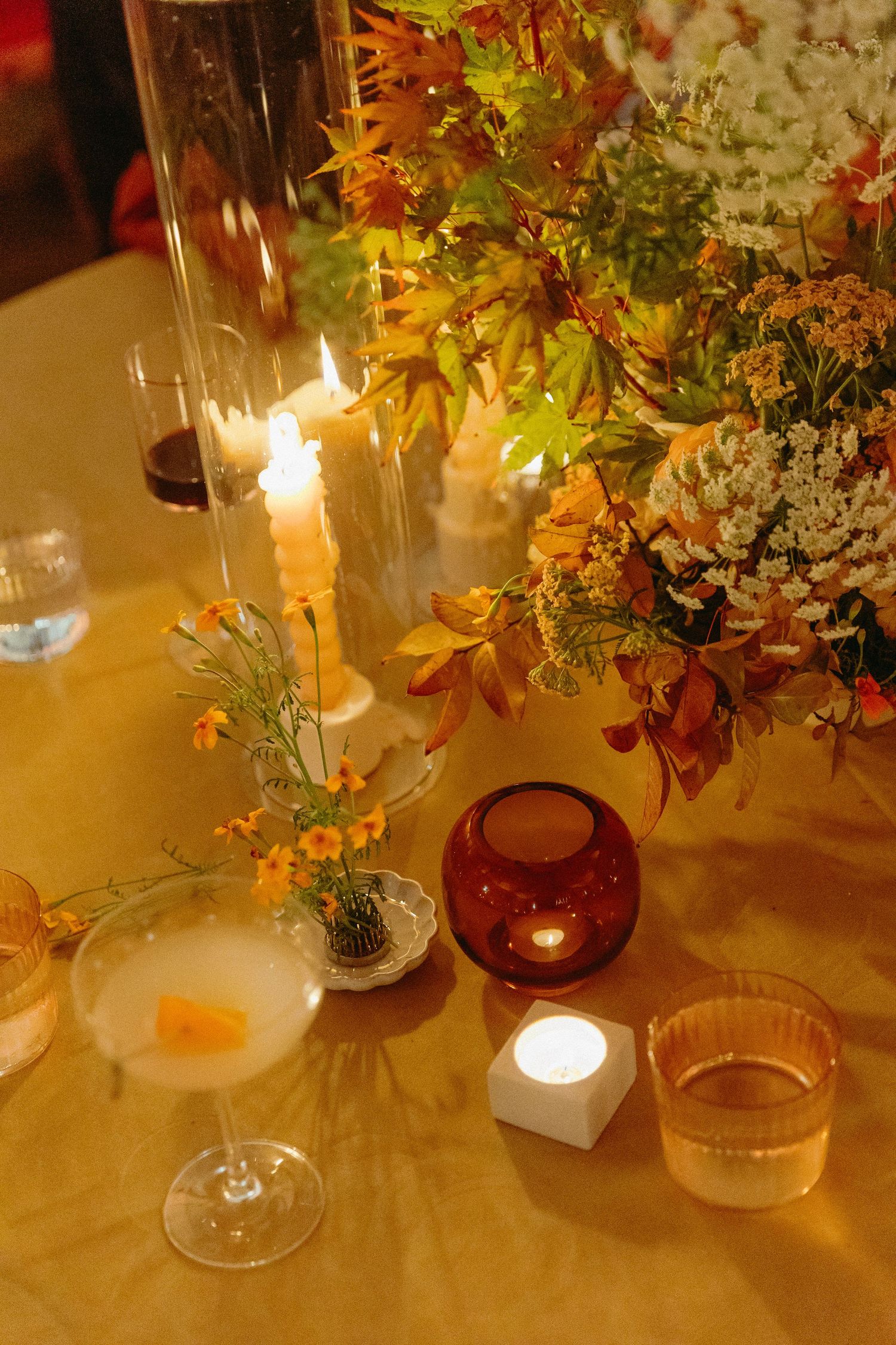 Elegant autumn table setting with cocktail, candles, and floral arrangement featuring orange and yellow fall leaves.