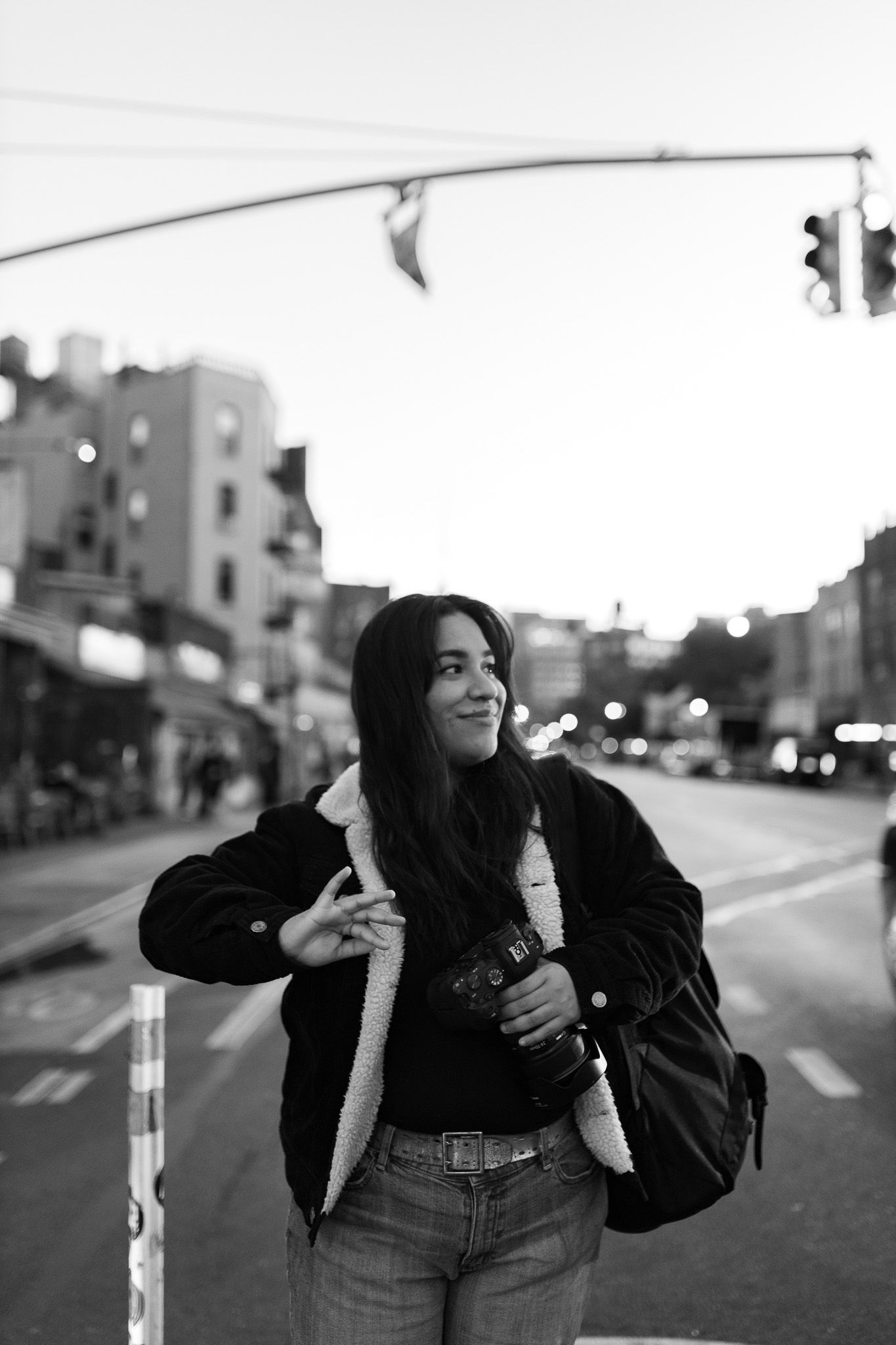 Black and white photo of woman holding camera on busy city street at twilight.