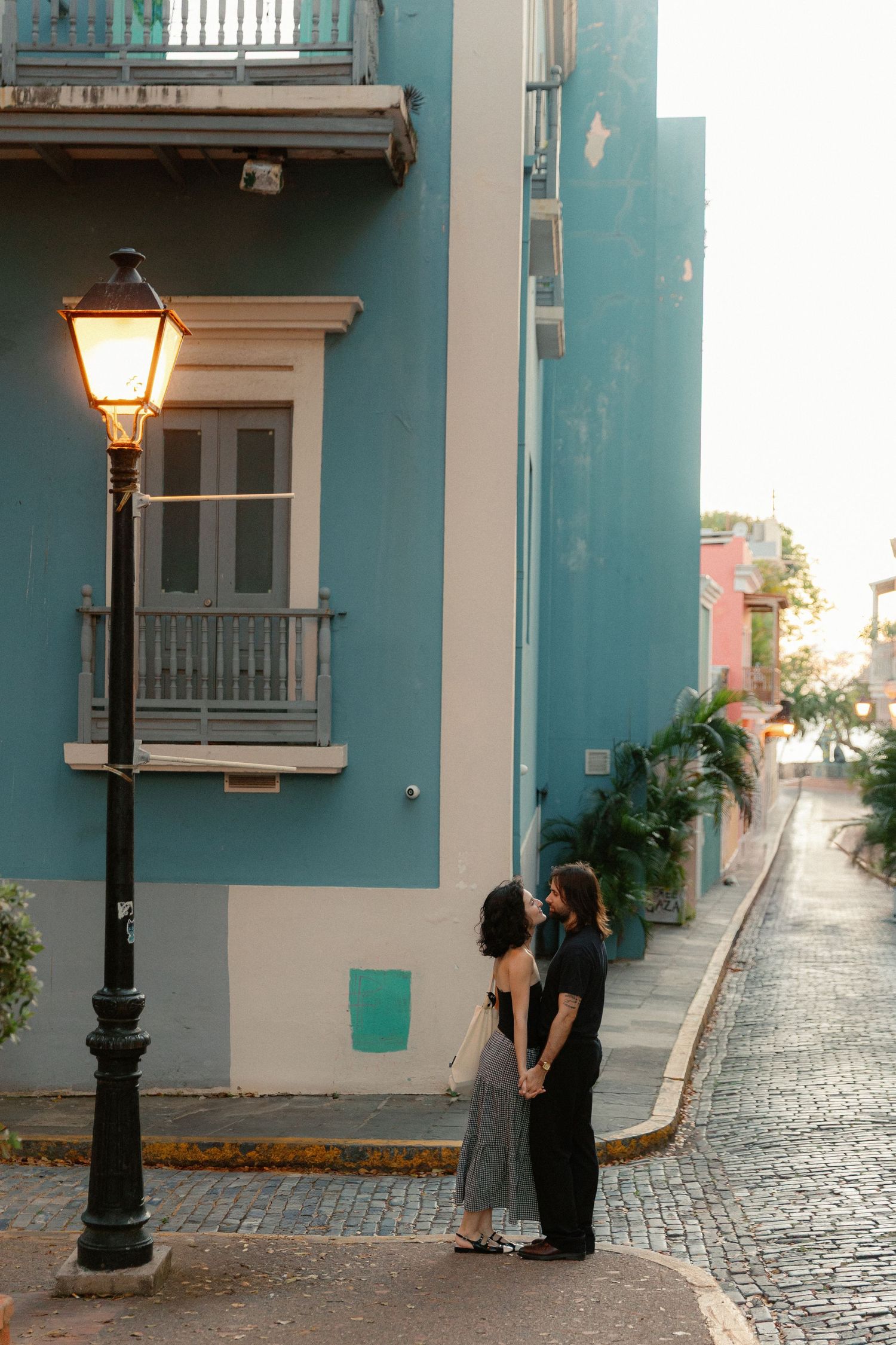 Couple holding hands facing each other on a cobblestone street beside a glowing lamp in Old San Juan.