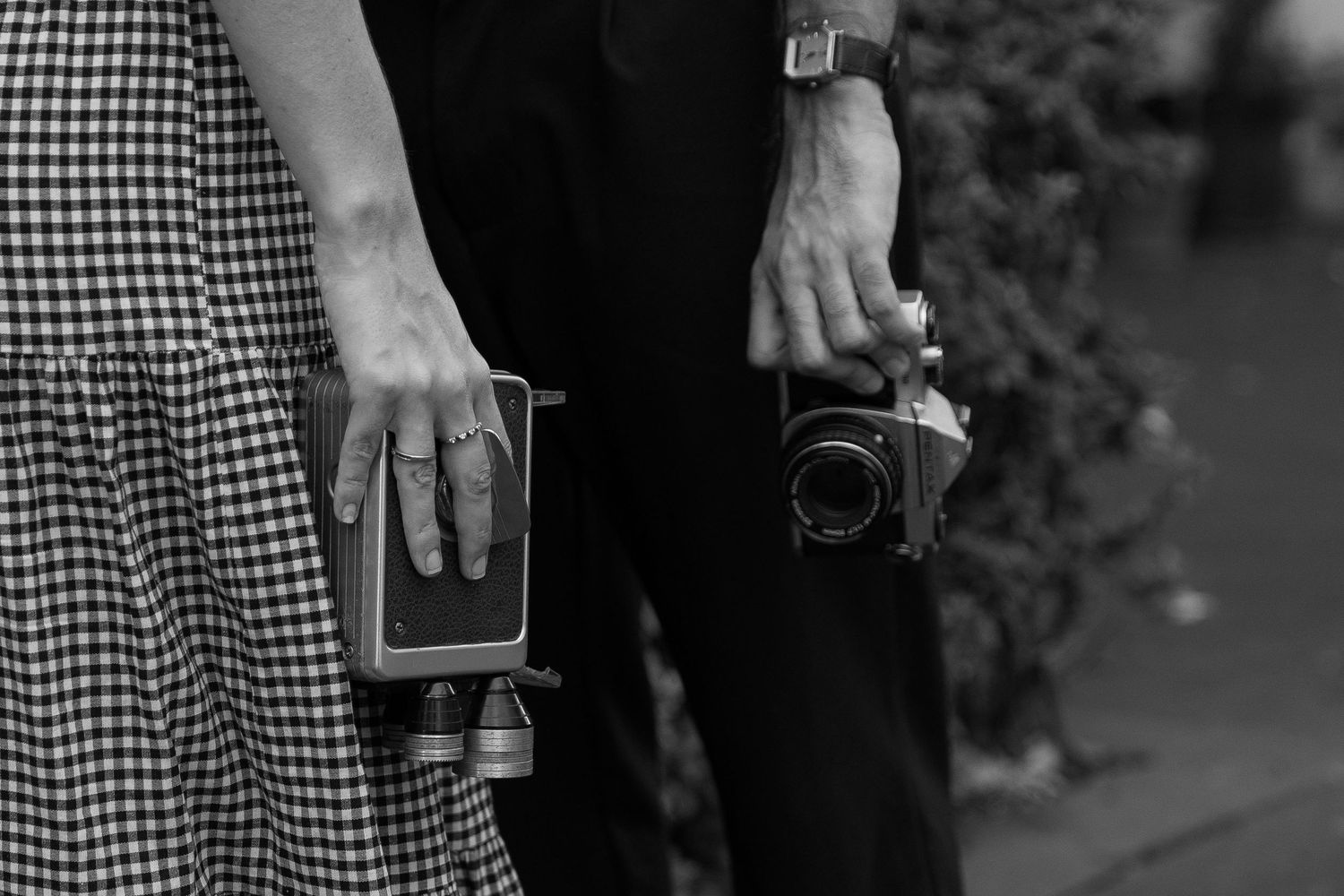 Black and white close-up of a couple holding a vintage camera and book at an outdoor wedding.