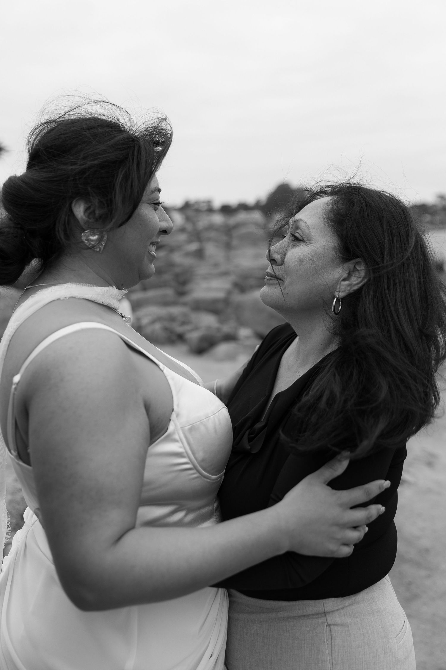 Two women embracing and smiling at each other outdoors in black and white photo.