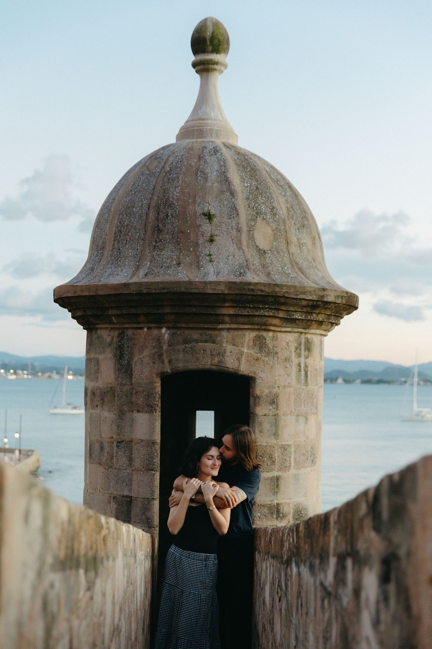 Historic stone watchtower with domed top overlooking a harbor filled with sailboats on a cloudy day.
