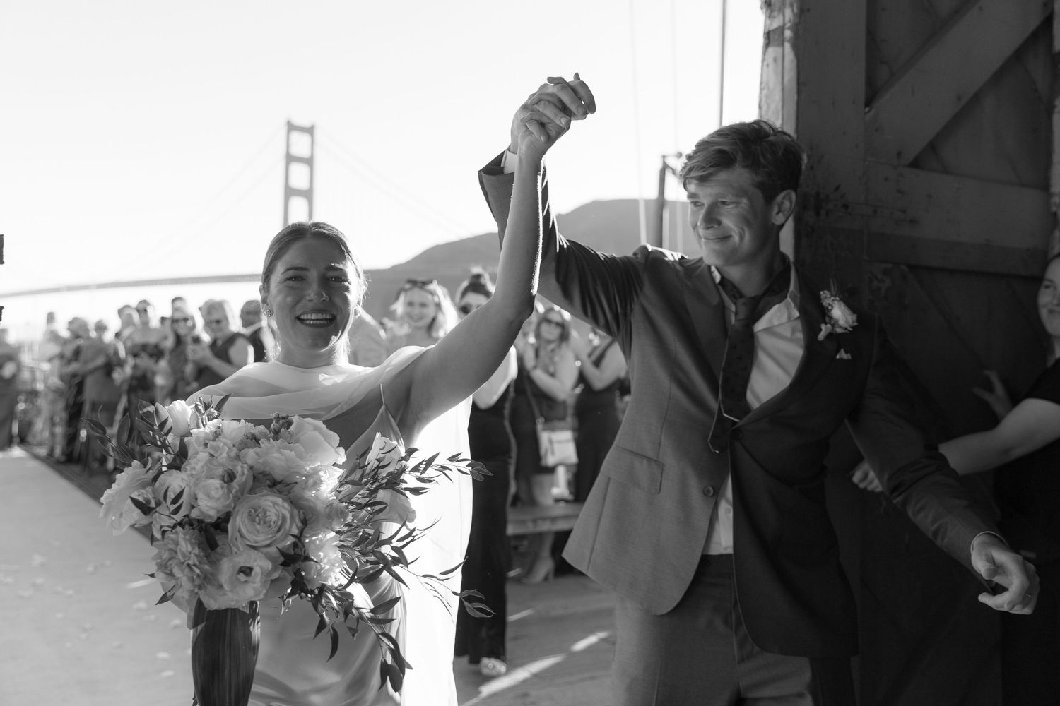 Happy bride and groom exit ceremony in black and white photo with Golden Gate Bridge behind them.